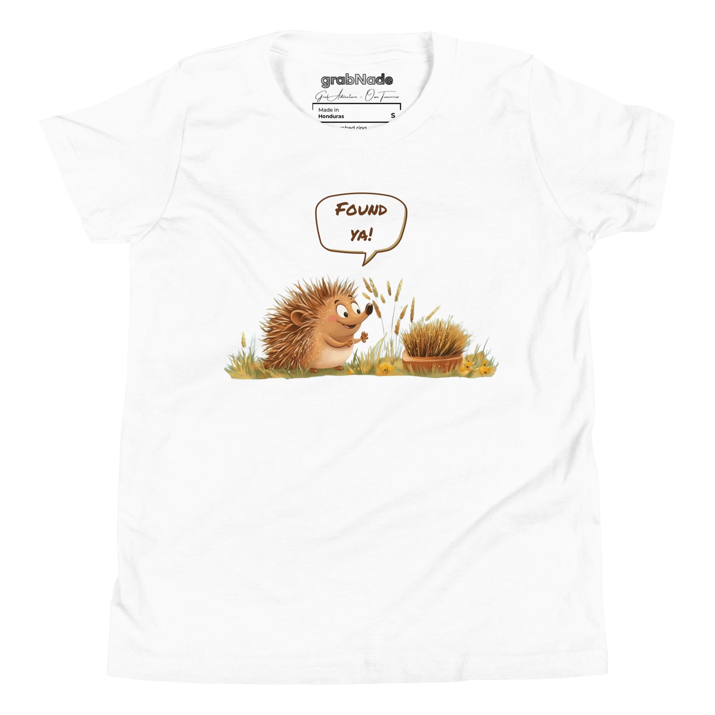 Product mockup. A smiling child wearing a light white t-shirt printed with a playful illustration of a cheerful hedgehog popping up from the grass and saying “Found ya!” in a speech bubble, beside a second hedgehog curled into a ball, all set against a clean studio background.