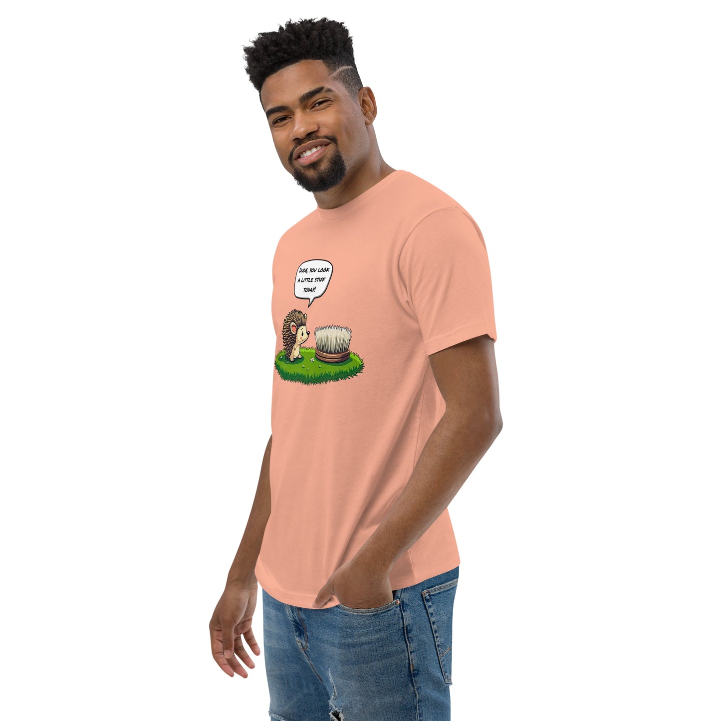 Product mockup. Man with short curly hair standing at an angle in a desert pink t-shirt and jeans, featuring a cartoon hedgehog talking to a brush and the same humorous caption.