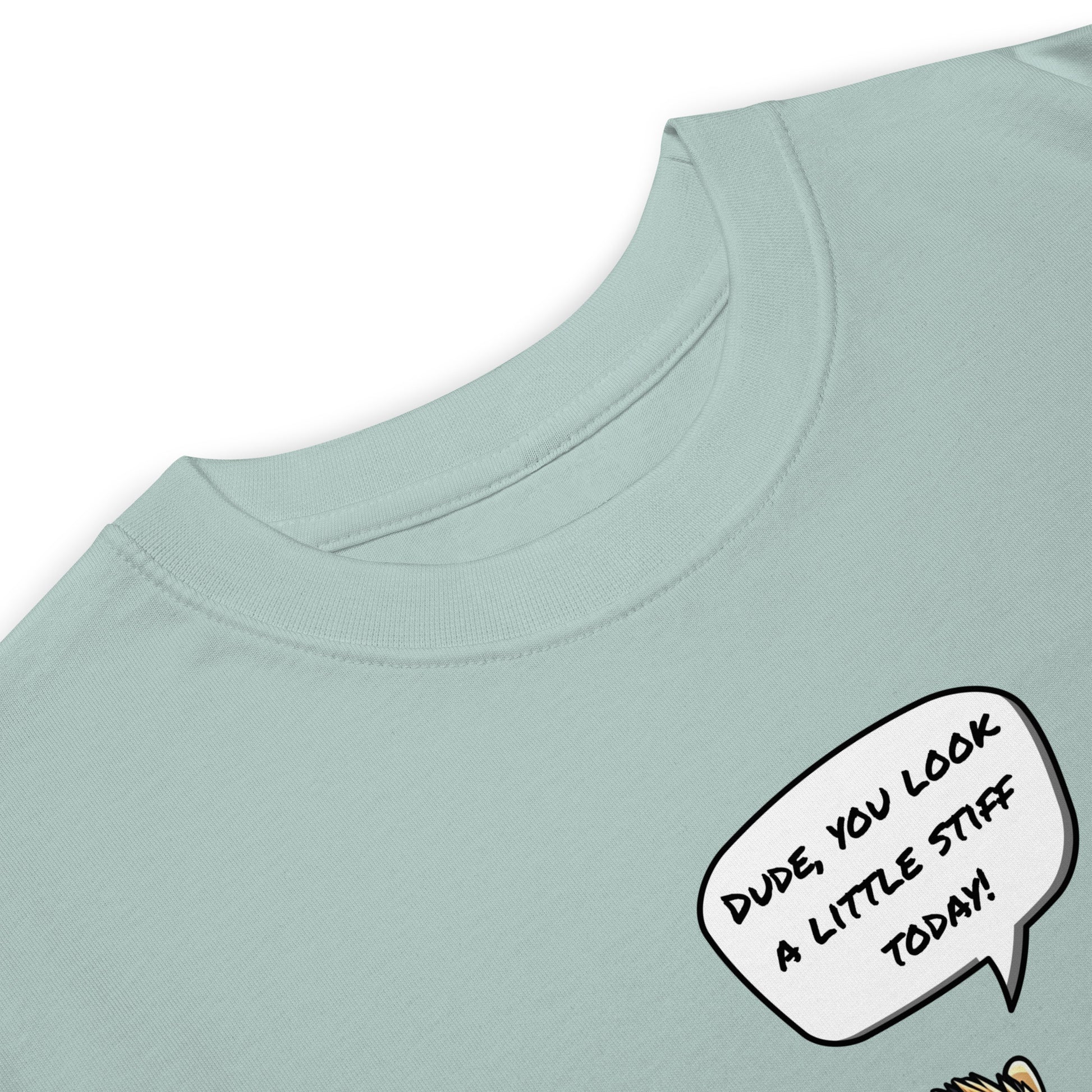 Close-up of the grabNade Men's Relaxed Heavyweight Tee in light blue premium cotton, featuring a comic speech bubble: "Dude you look a little stiff today." Only the top portion and part of a cartoon character are visible.