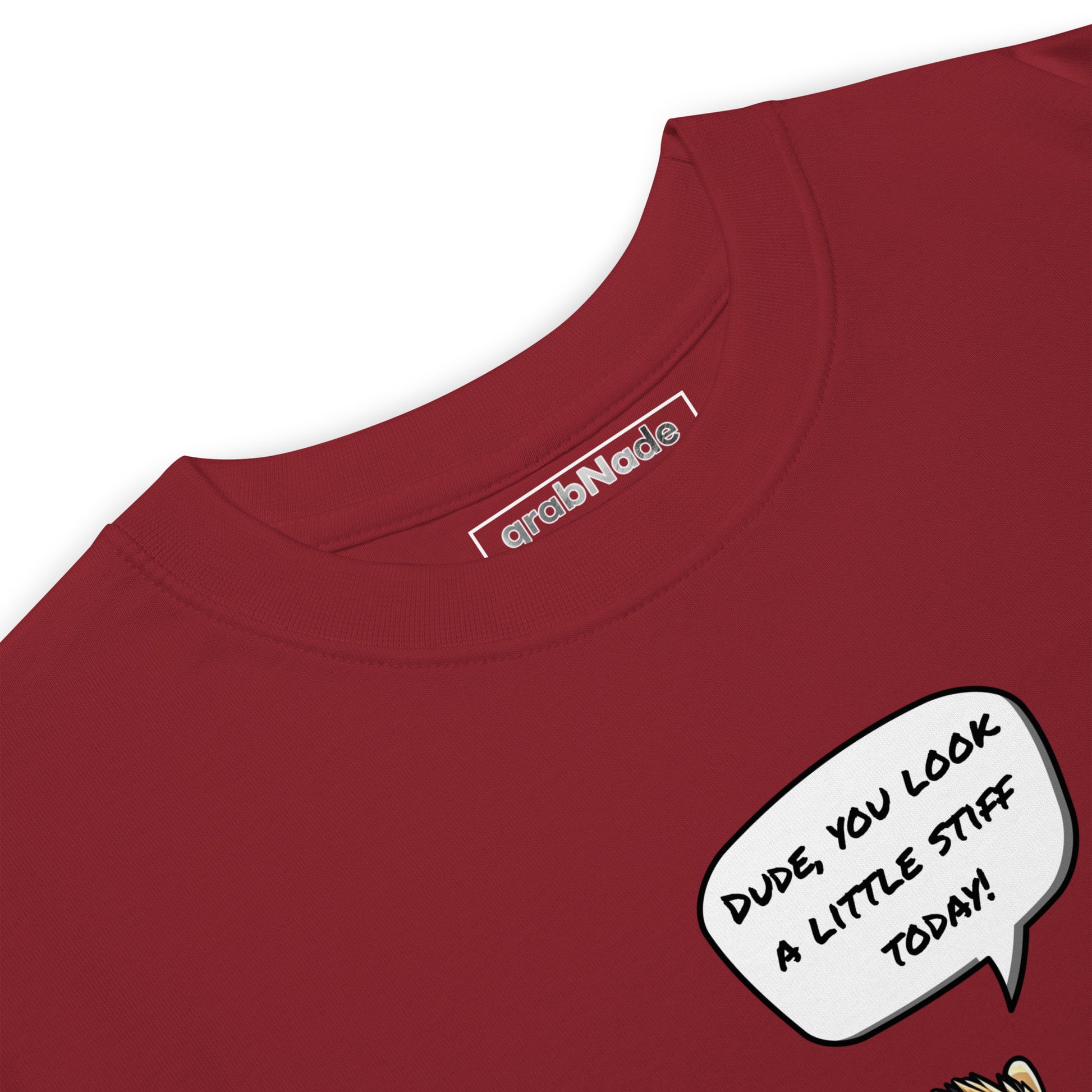 A close-up of the grabNade Men's Relaxed Heavyweight Tee in premium cotton shows its label inside the collar and a comic-style speech bubble on the shirt reading, "DUDE, YOU LOOK A LITTLE STIFF TODAY!" in bold black on white.