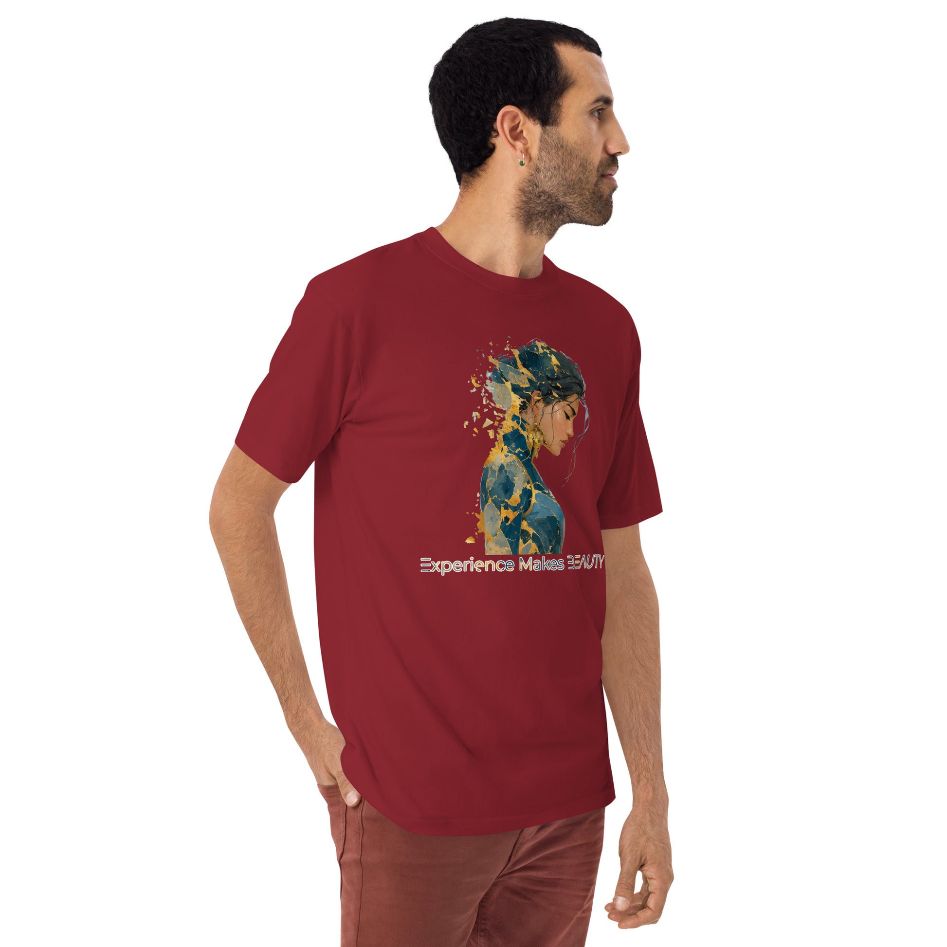 Product mockup. Man with short curly hair standing at an angle in a brick-red heavyweight t-shirt and brick-colored pants, with a side-silhouette female portrait, gold paint splatter effect, and the words "Experience Makes BEAUTY."