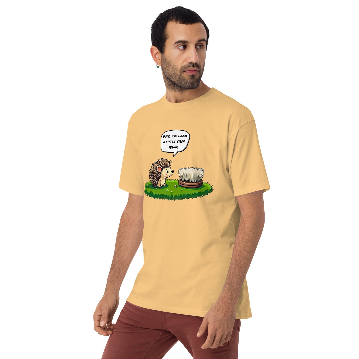 Product mockup. Man with short curly hair and an earring standing at an angle in a pale yellow t-shirt and brick-colored pants, with a cartoon hedgehog talking to a brush and the caption "Dude, you look a little stiff today!"