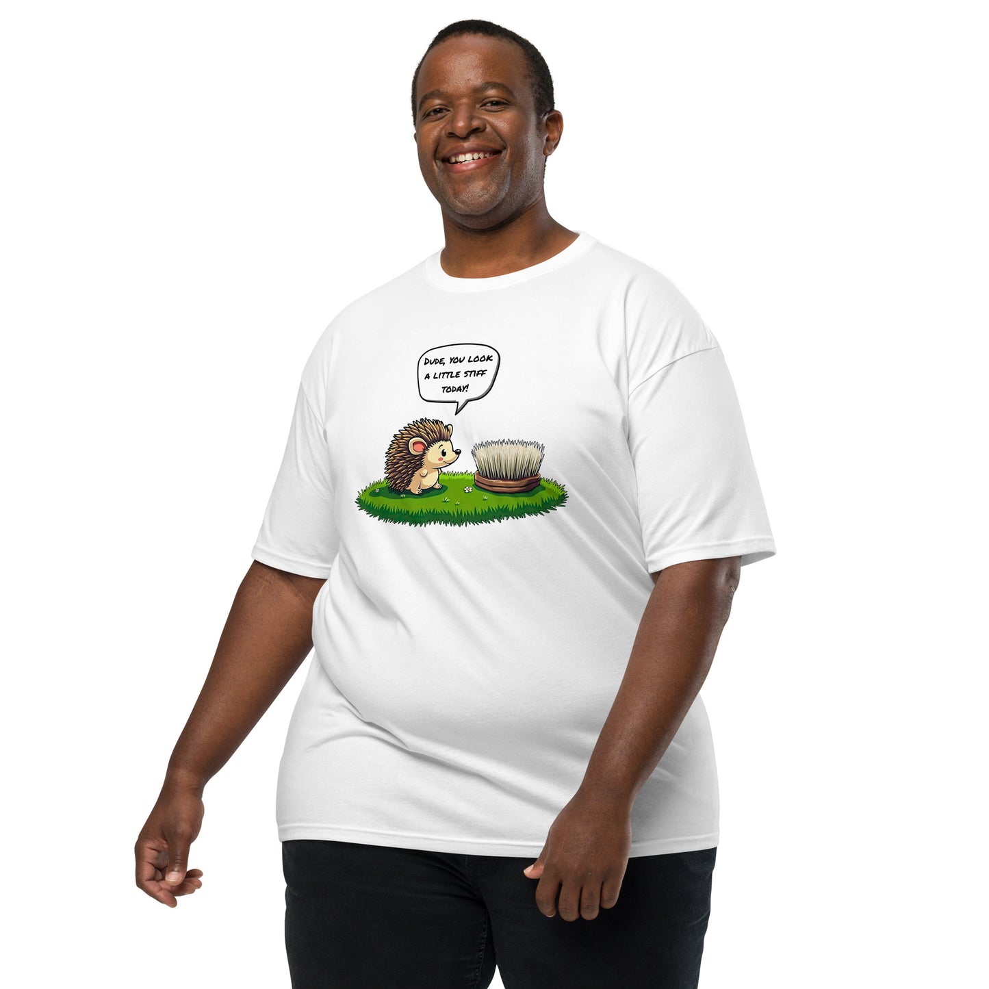 A smiling man wears the grabNade Men's Relaxed Heavyweight Tee in premium cotton, featuring a cartoon hedgehog facing a hairbrush on grass with the text "Dude you look a little stiff today," set against a plain white background.