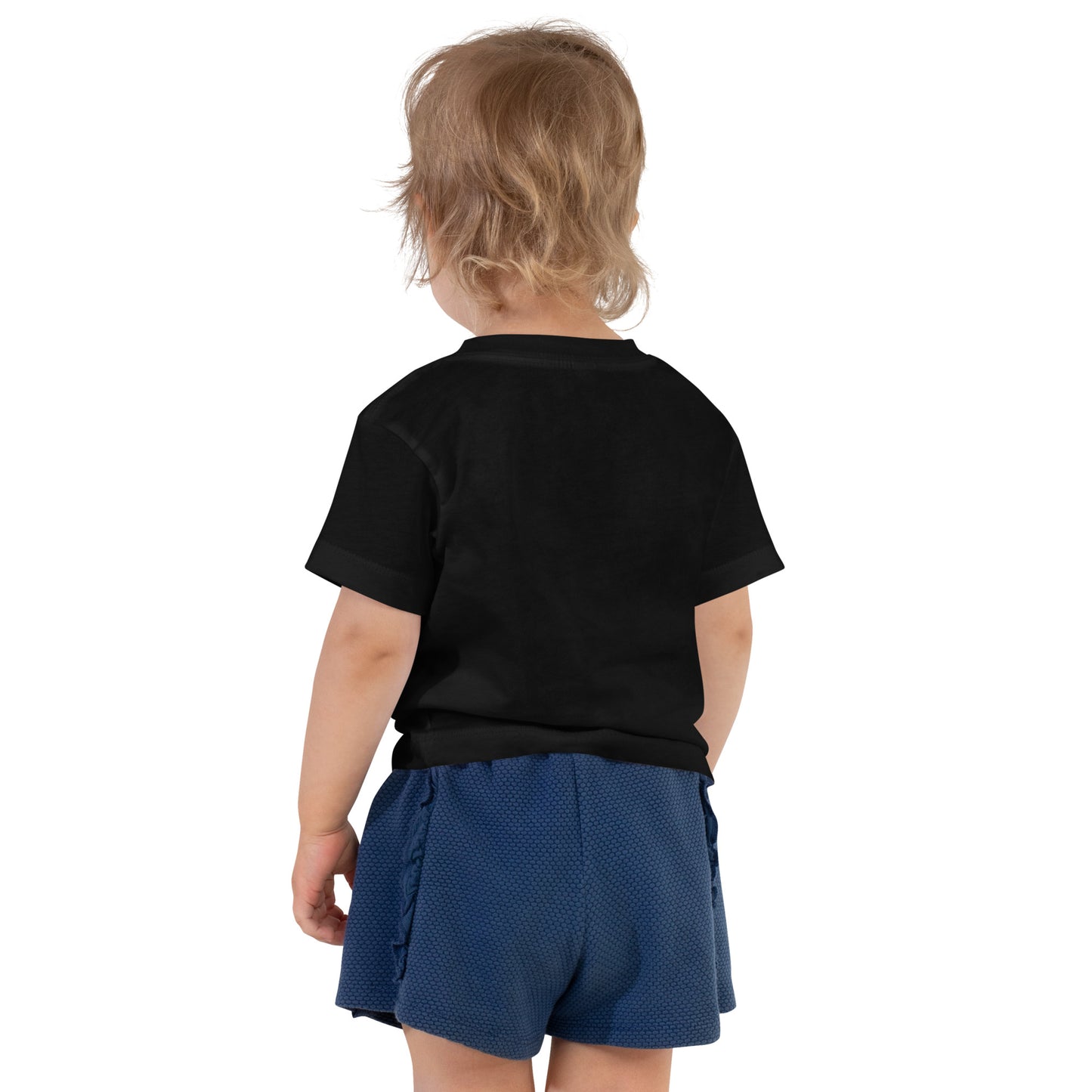 Product mockup. A toddler seen from behind, wearing a plain black short-sleeve t-shirt and textured navy blue shorts. The child's hair is medium length and slightly tousled, and no designs are visible on the back of the shirt.