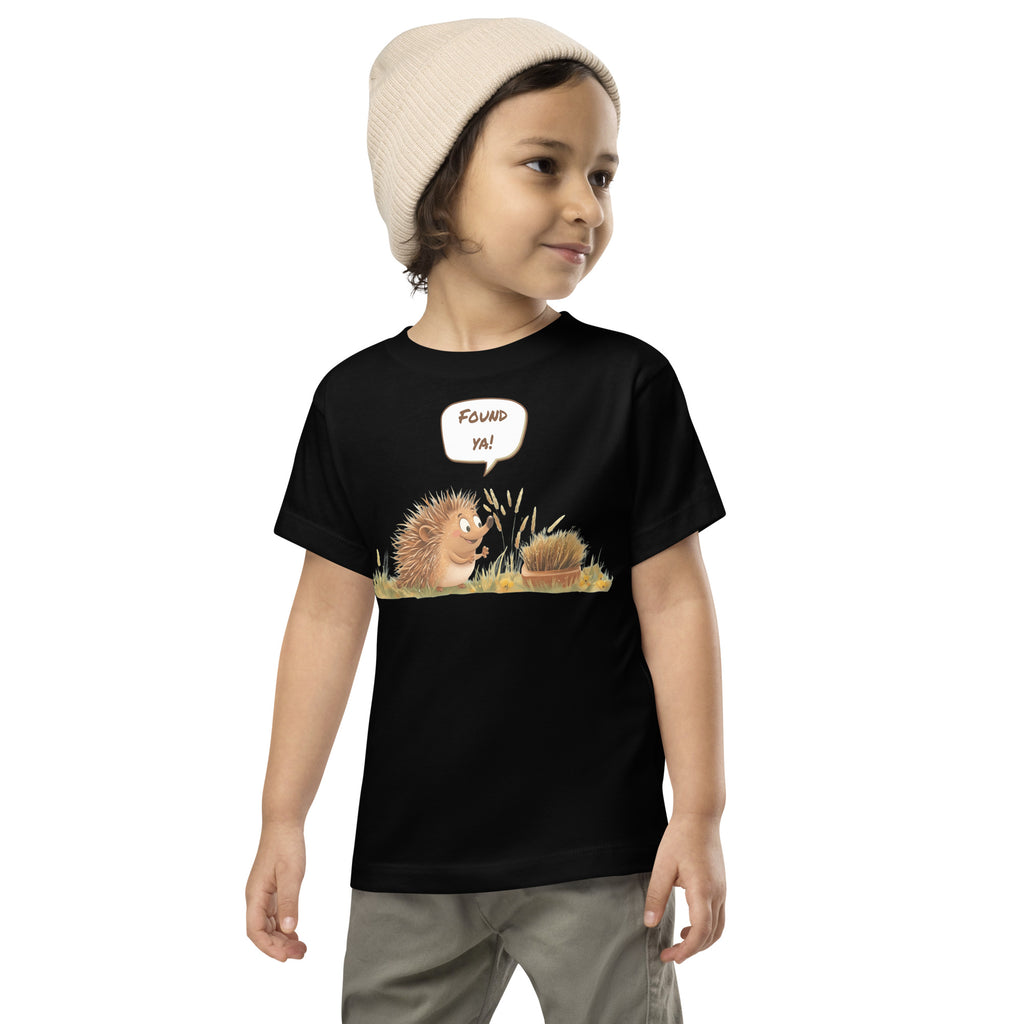 Product mockup. Toddler standing, wearing a black t-shirt with a blue, yellow, and green smiley face centered on the chest.