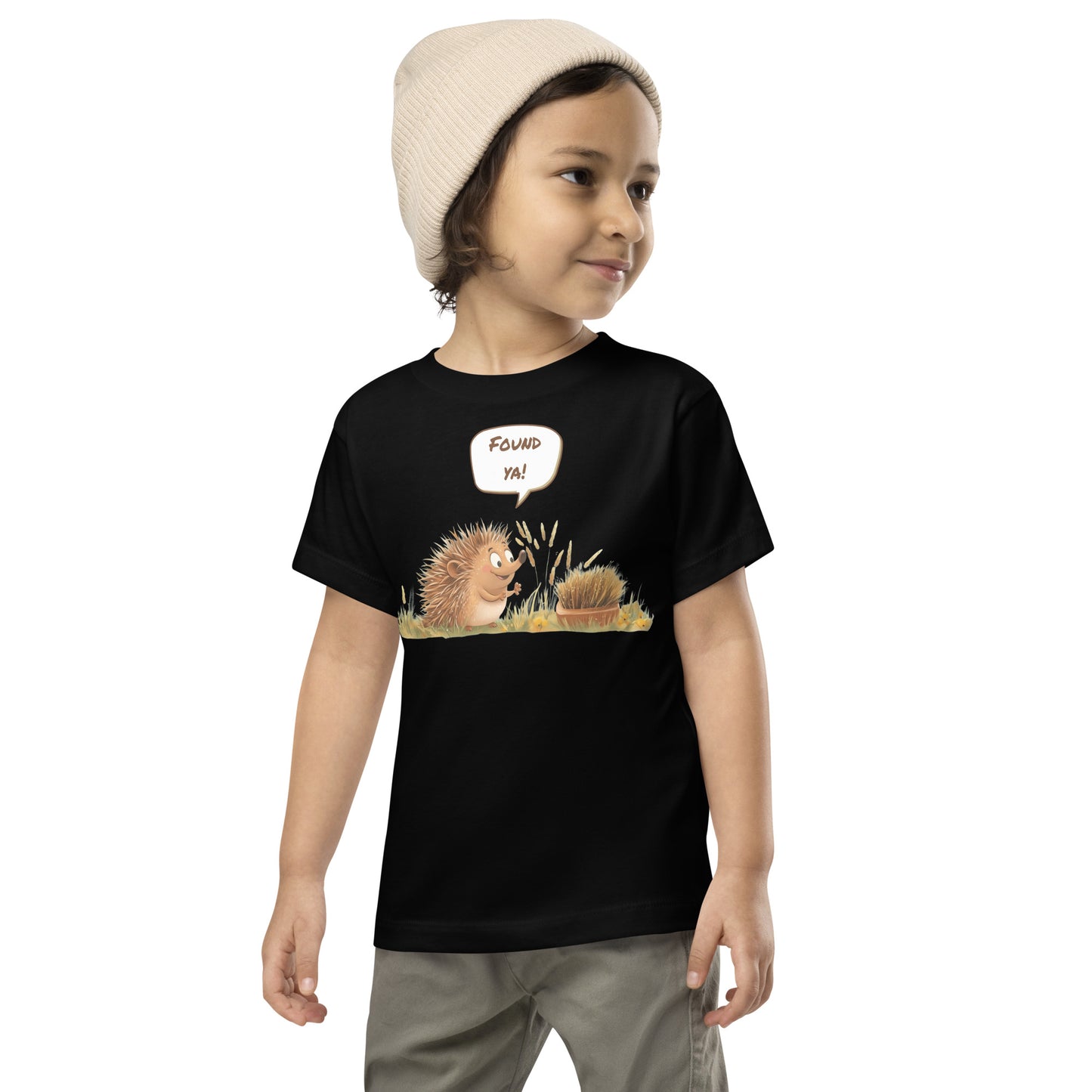 Product mockup. Toddler standing, wearing a black t-shirt with a blue, yellow, and green smiley face centered on the chest.