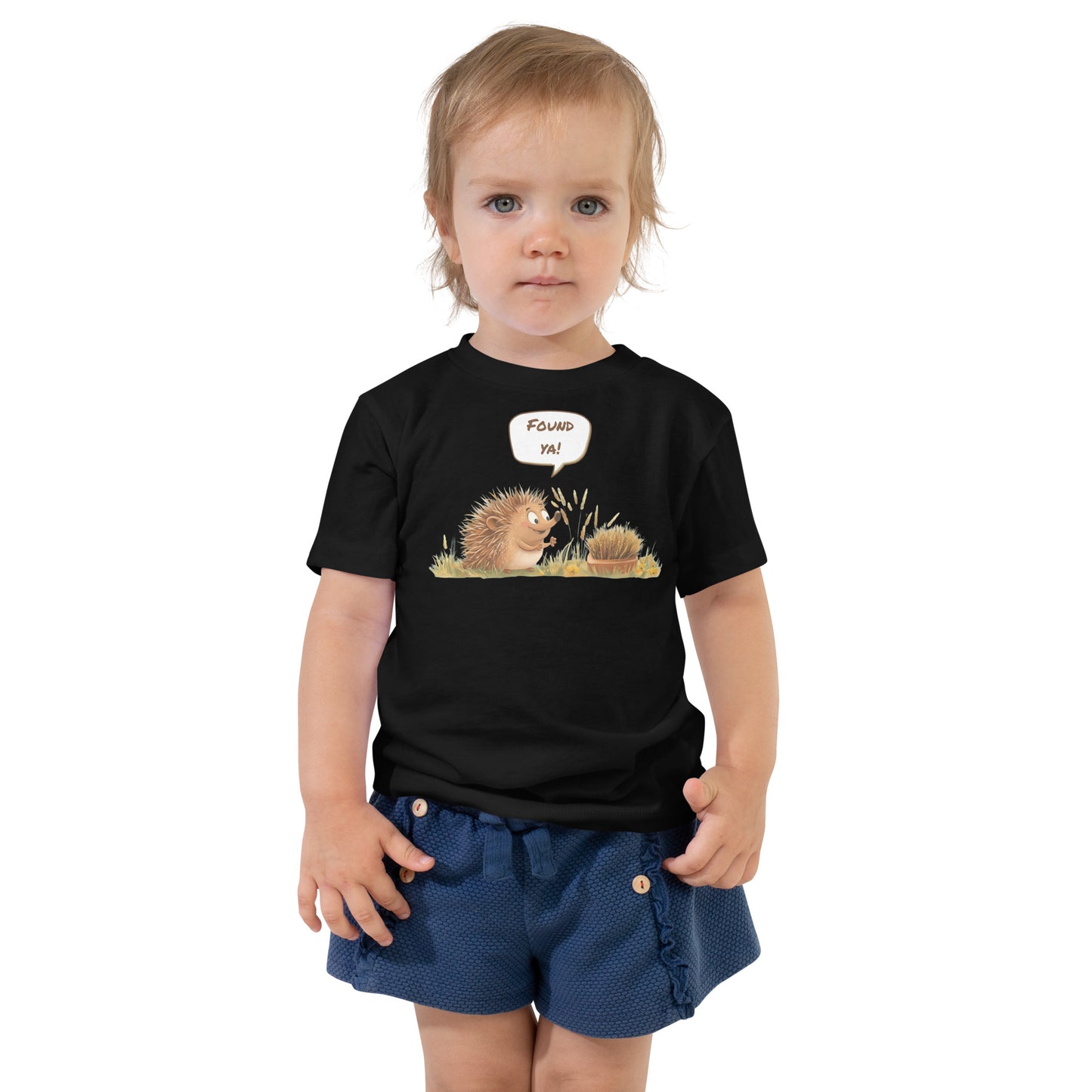 Product mockup. Toddler standing, wearing a black t-shirt with a blue, yellow, and green smiley face centered on the chest.