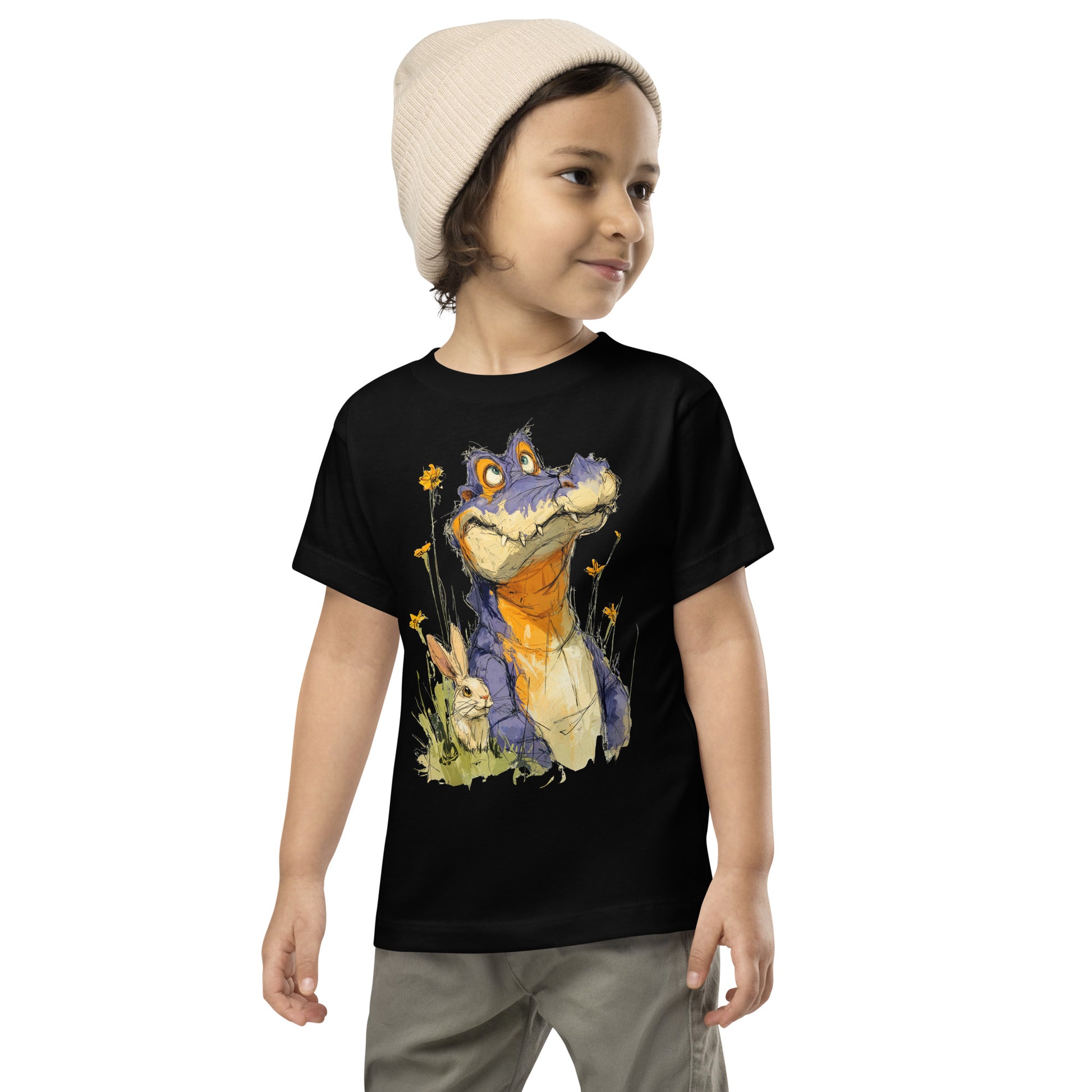Product mockup. A young child wearing a light beige knit beanie and a black t-shirt with a large, whimsical illustration of a friendly purple and orange cartoon dinosaur surrounded by yellow wildflowers, with a small rabbit nestled in the grass near its feet.
