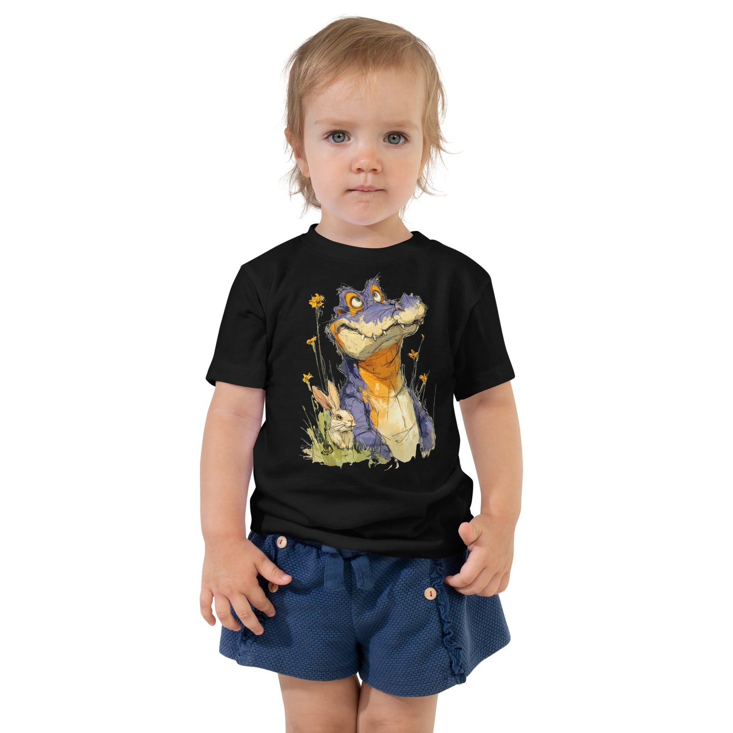 Product mockup. A toddler wearing navy blue textured shorts and a black t-shirt featuring a whimsical illustration of a purple and orange cartoon dinosaur among yellow wildflowers, with a small rabbit sitting in the grass beside it.