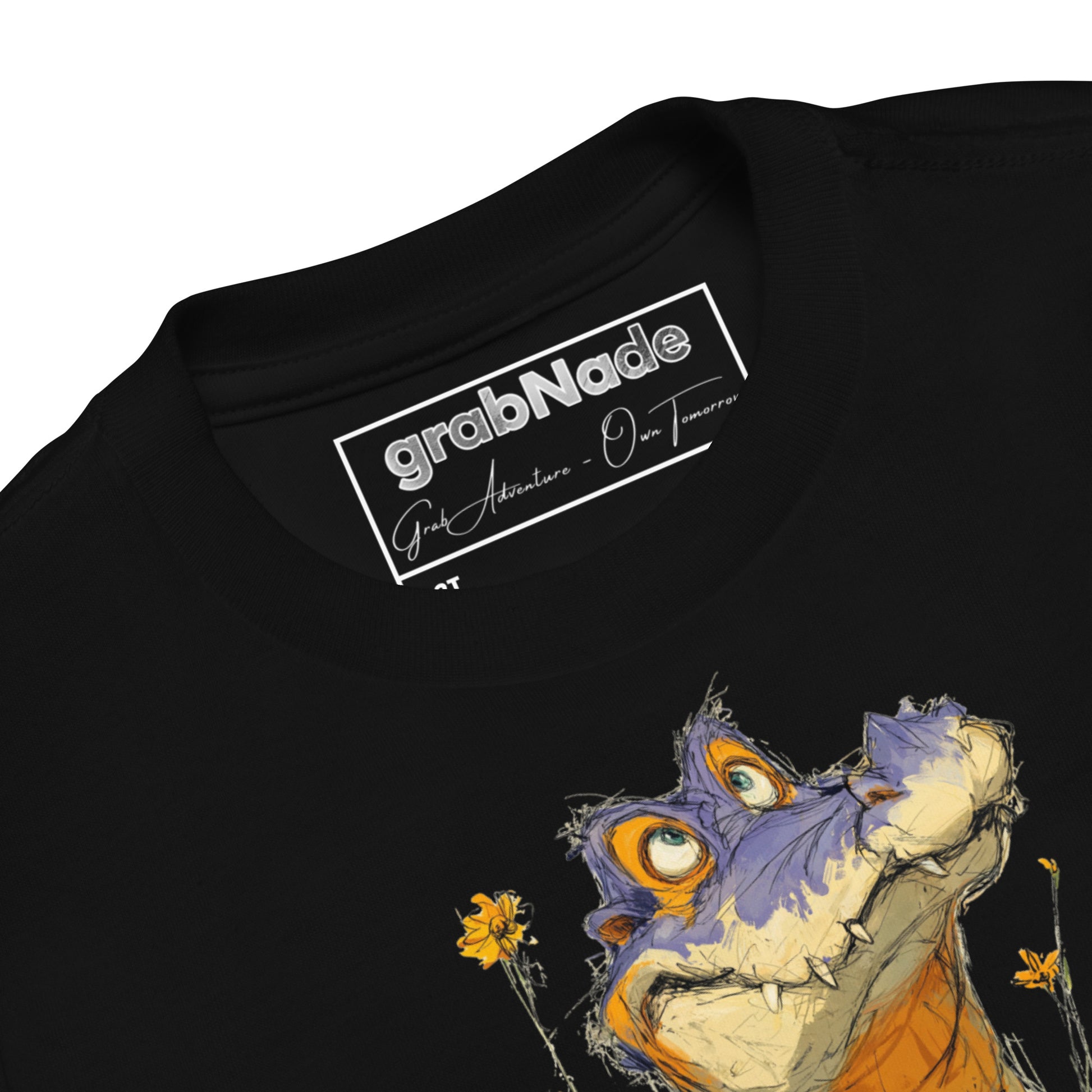 Product mockup. Close-up view of a black t-shirt collar showing the 'grabNade' brand label inside the neckline, with handwritten-style text beneath the brand name reading 'Grab Adventure - Own Tomorrow.' The shirt features part of a colorful cartoon illustration of a purple and orange dinosaur and yellow flowers visible below the collar.