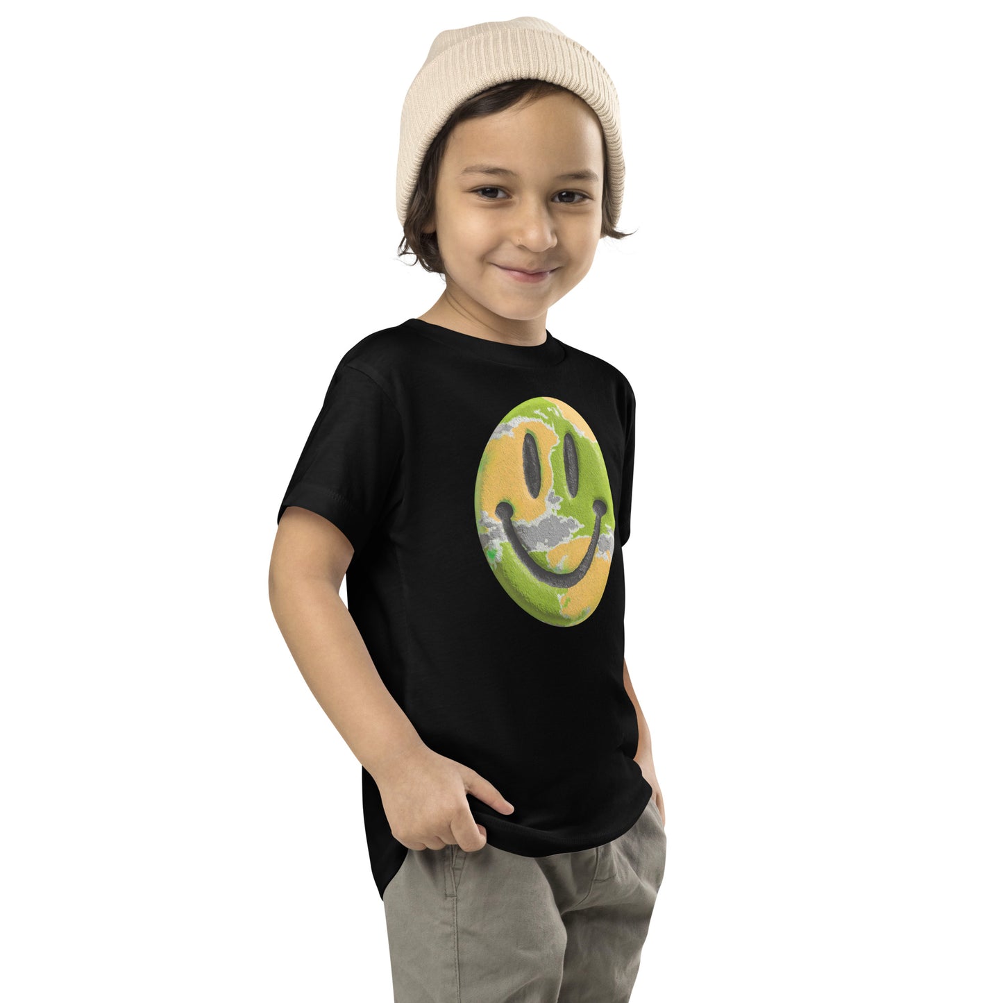 Product mockup. Child standing sideways, wearing a black t-shirt with a large pink, yellow, and blue smiley face icon, khaki pants, and a beige knit hat.