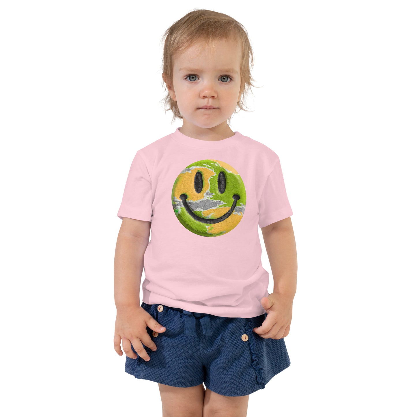 Product mockup. Toddler's light pink t-shirt laid flat, centered with a blue, yellow, and green smiley face graphic.