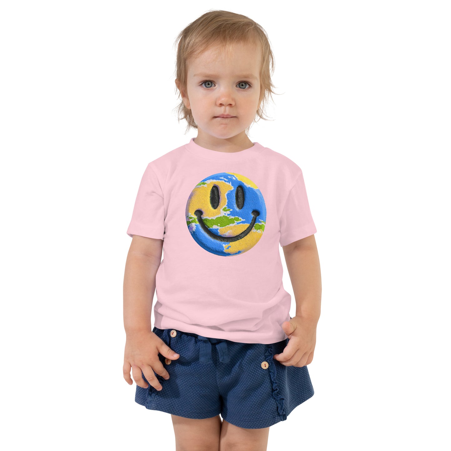Product mockup. Toddler's light pink t-shirt laid flat, centered with a blue, yellow, and green smiley face graphic.