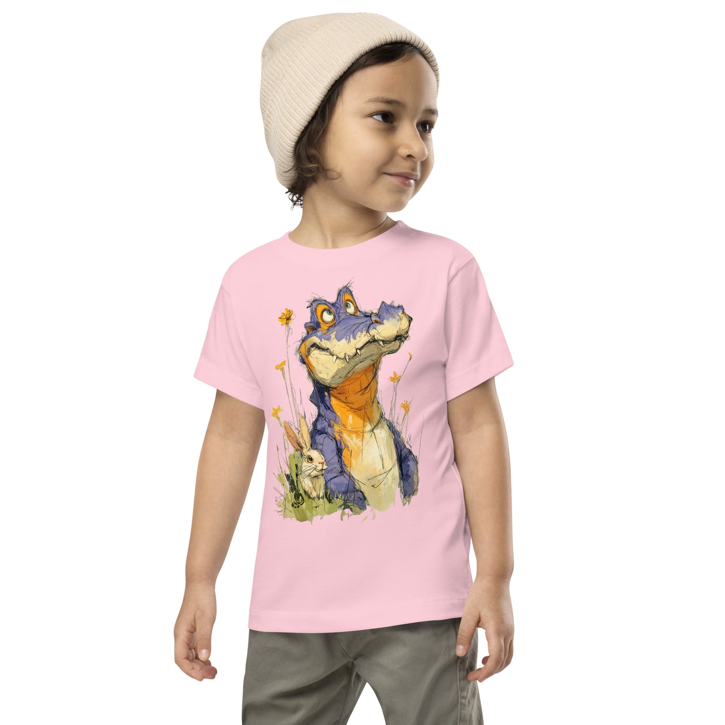 Product mockup. A young child wearing a light beige knit beanie and a light pink t-shirt with a large, whimsical illustration of a friendly purple and orange cartoon dinosaur surrounded by yellow wildflowers, with a small rabbit nestled in the grass near its feet.