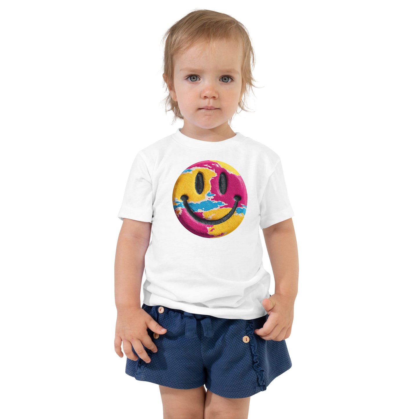 Product mockup. Toddler standing, wearing a white t-shirt with a large blue, yellow, and green smiley face icon, and blue jeans.