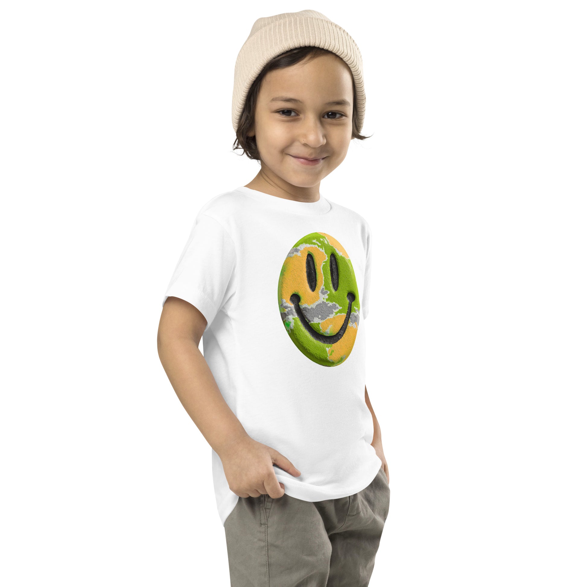 Product mockup. Child standing sideways, wearing a white t-shirt with a green and yellow smiley face icon, khaki pants, and beige hat.