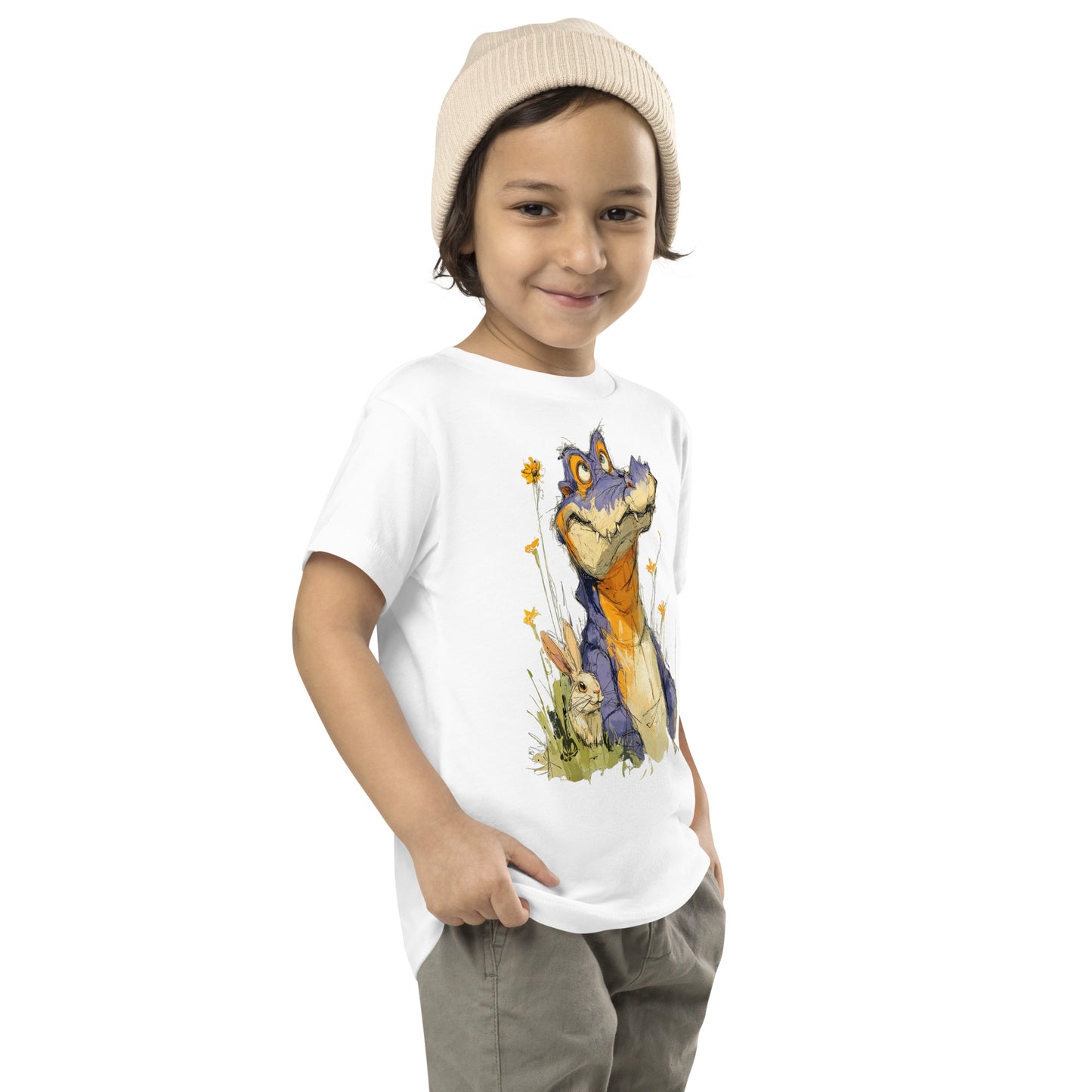 Product mockup. A young child wearing a light beige knit beanie and a white t-shirt with a large, whimsical illustration of a friendly purple and orange cartoon dinosaur surrounded by yellow wildflowers, with a small rabbit nestled in the grass near its feet.