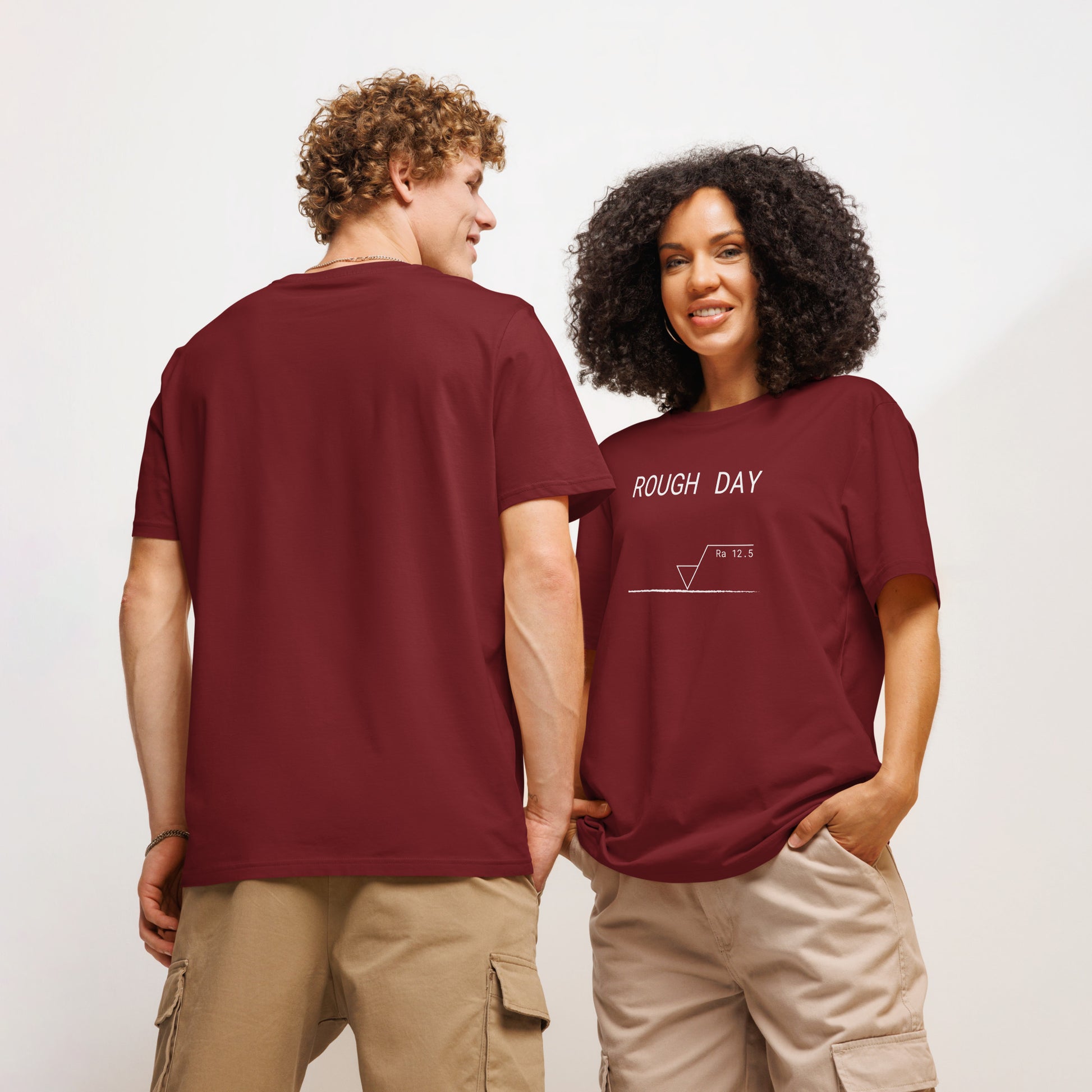 Man seen from behind and woman facing forward wearing red GOTS organic tee with white roughness symbol and "ROUGH DAY (Ra 12.5)" text.