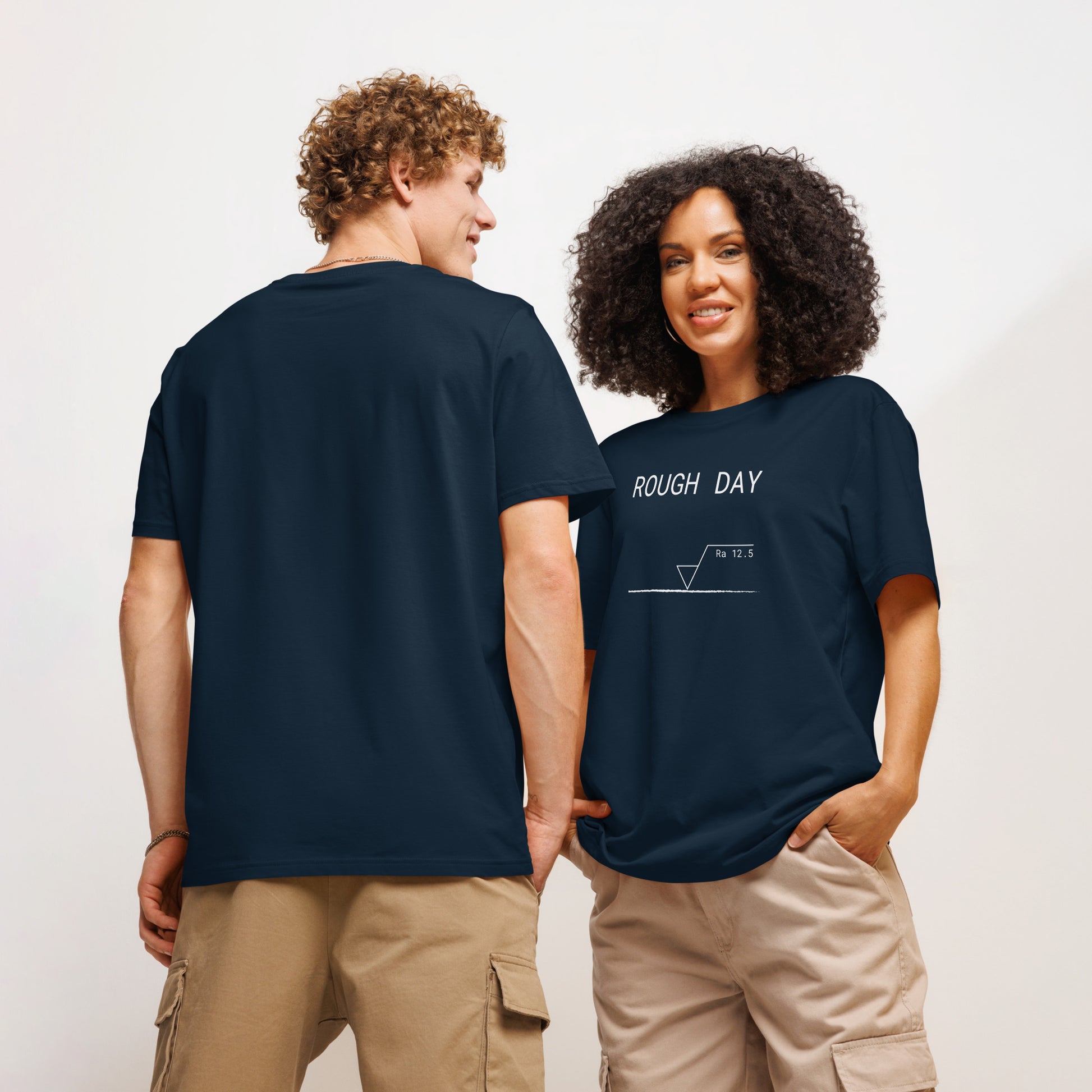 Man seen from behind and woman facing forward wearing navy GOTS organic tee with white roughness symbol and "ROUGH DAY (Ra 12.5)" text.