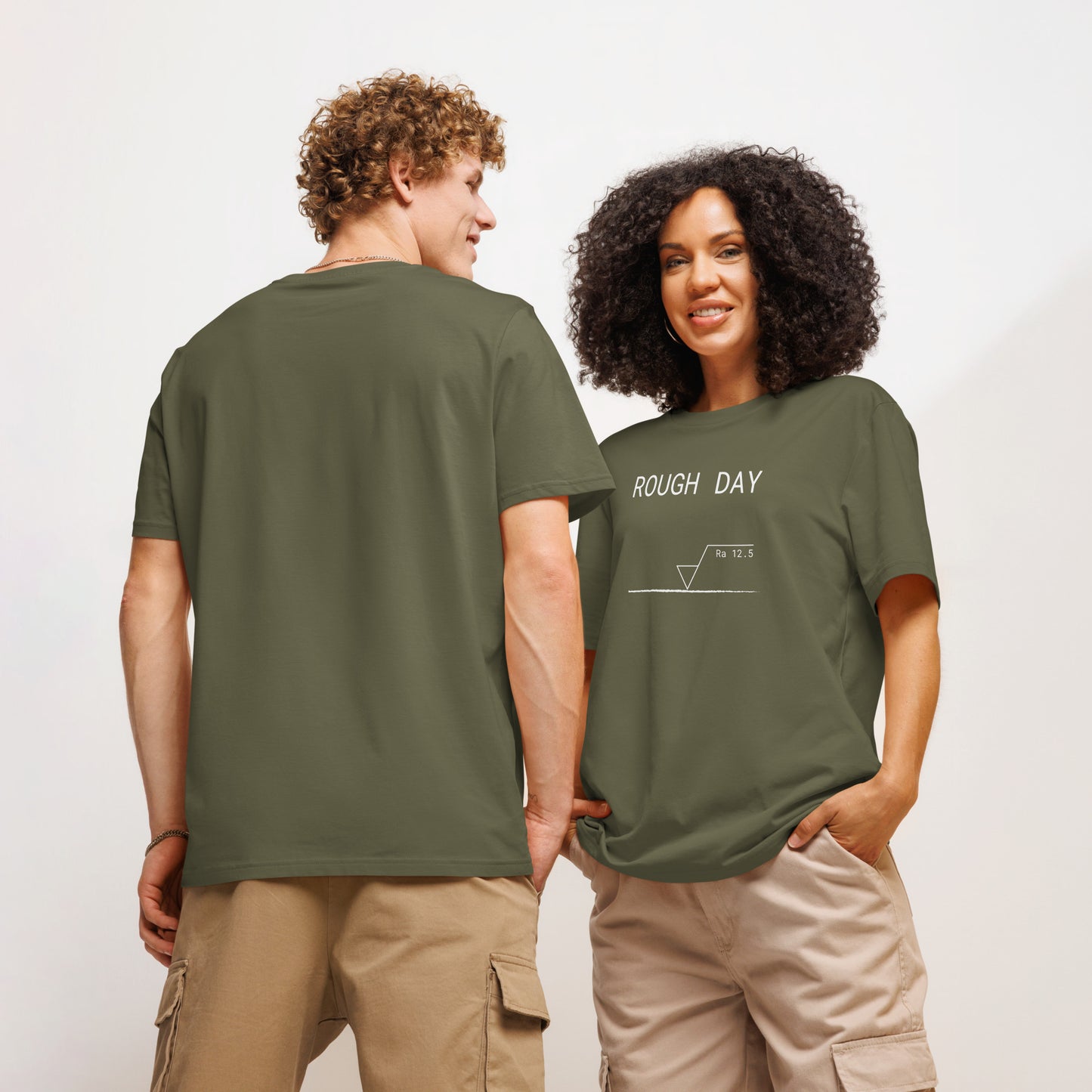 Man seen from behind and woman facing forward wearing green GOTS organic tee with white roughness symbol and "ROUGH DAY (Ra 12.5)" text.