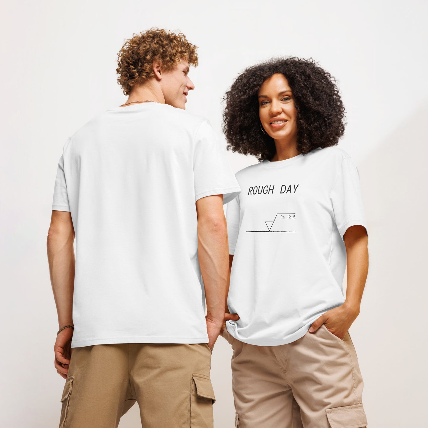 Man seen from behind and woman facing forward wearing white GOTS organic tee with roughness symbol and "ROUGH DAY (Ra 12.5)" text.