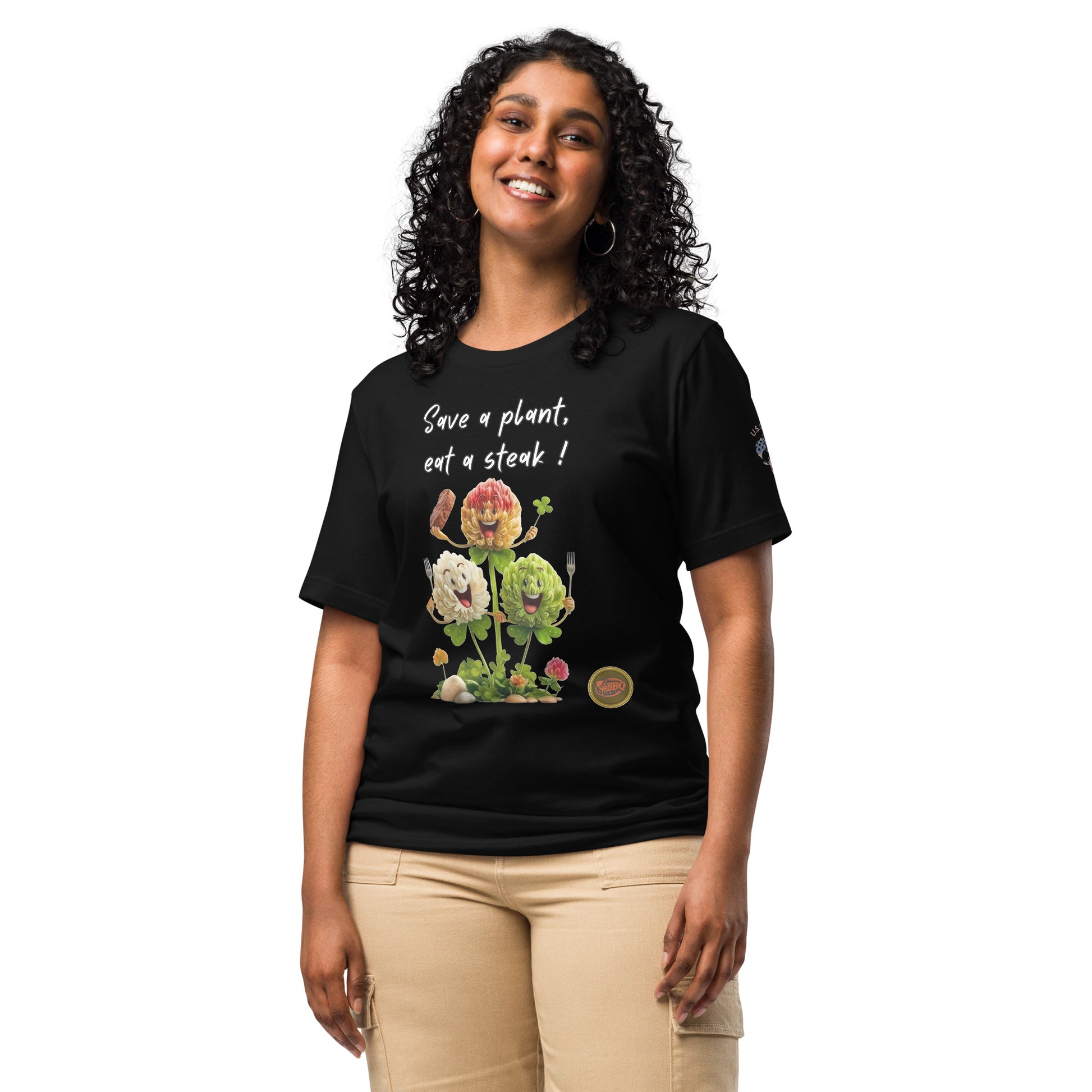 Product mockup. A woman stands wearing a black t-shirt with "Save a plant, eat a steak!" written above a cartoon image of three cheerful flowers holding utensils and steak.