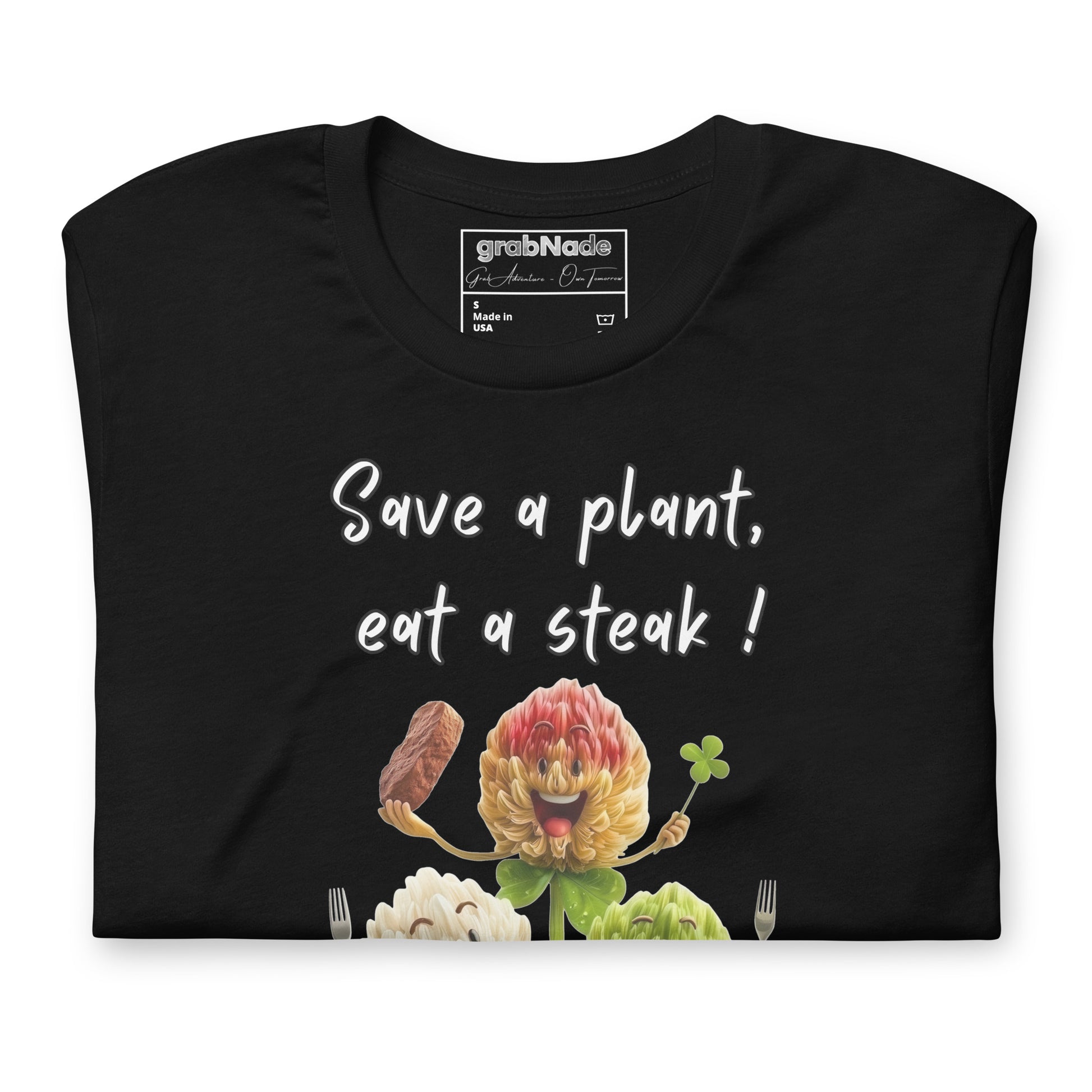Product mockup. Black t-shirt folded, front visible with the design "Save a plant, eat a steak!" above a cartoon cloverv holding a steak and a clover.