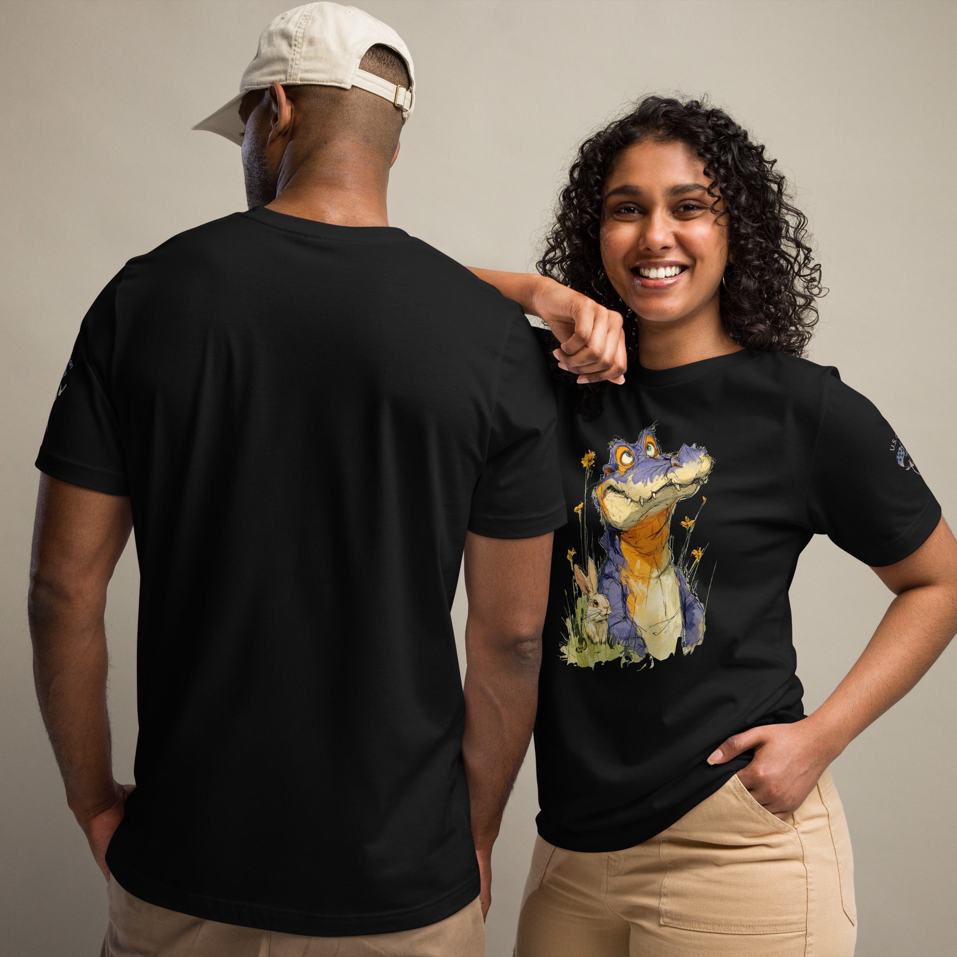 Product mockup. A man and woman stand together; the woman wears a black t-shirt with a large fun illustration of an alligator in a field, while the man shows the back of a plain black t-shirt.
