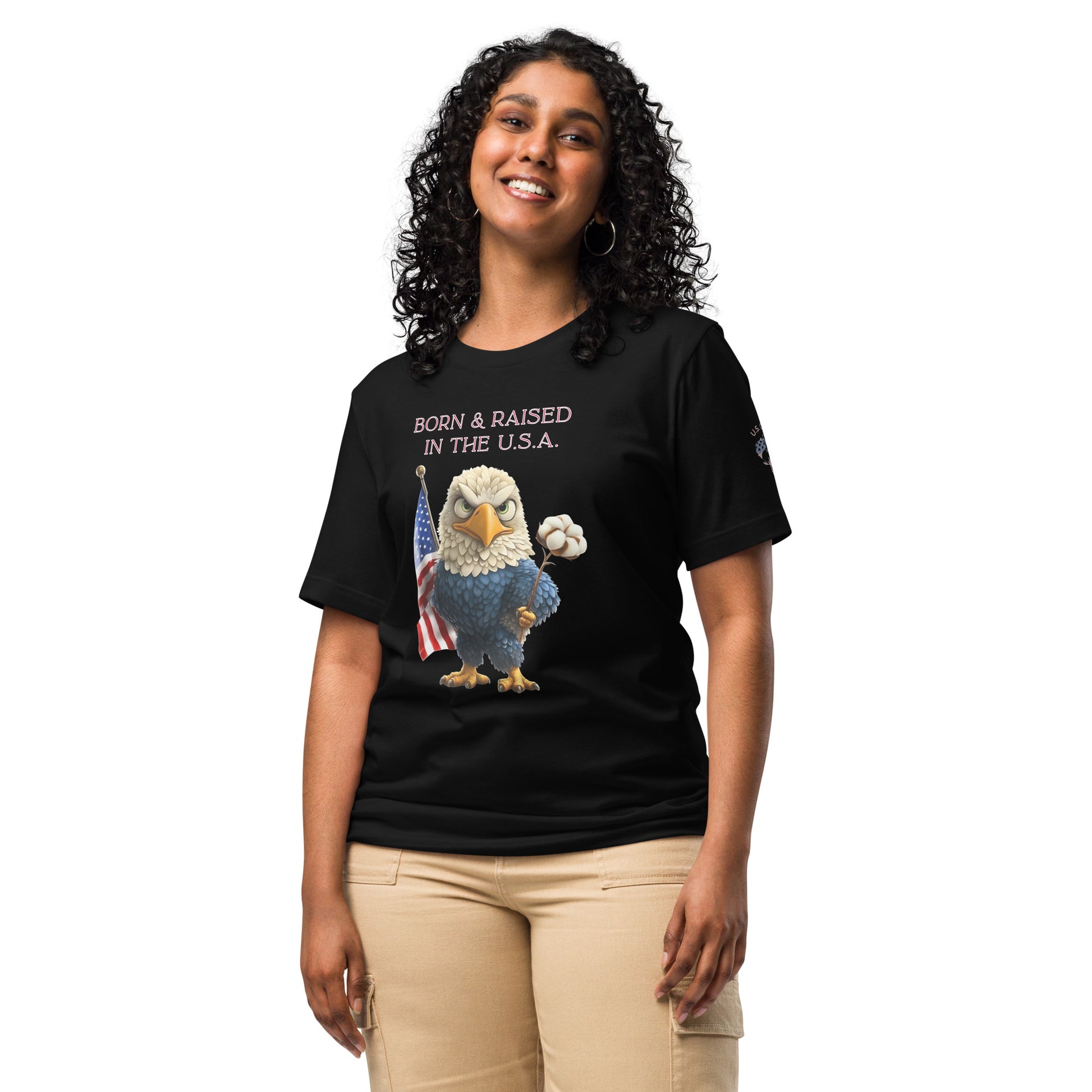 Product mockup. A woman stands wearing a black t-shirt with a cartoon bald eagle holding a cotton flower and standing by an American flag, above the phrase "Born & Raised in the U.S.A."