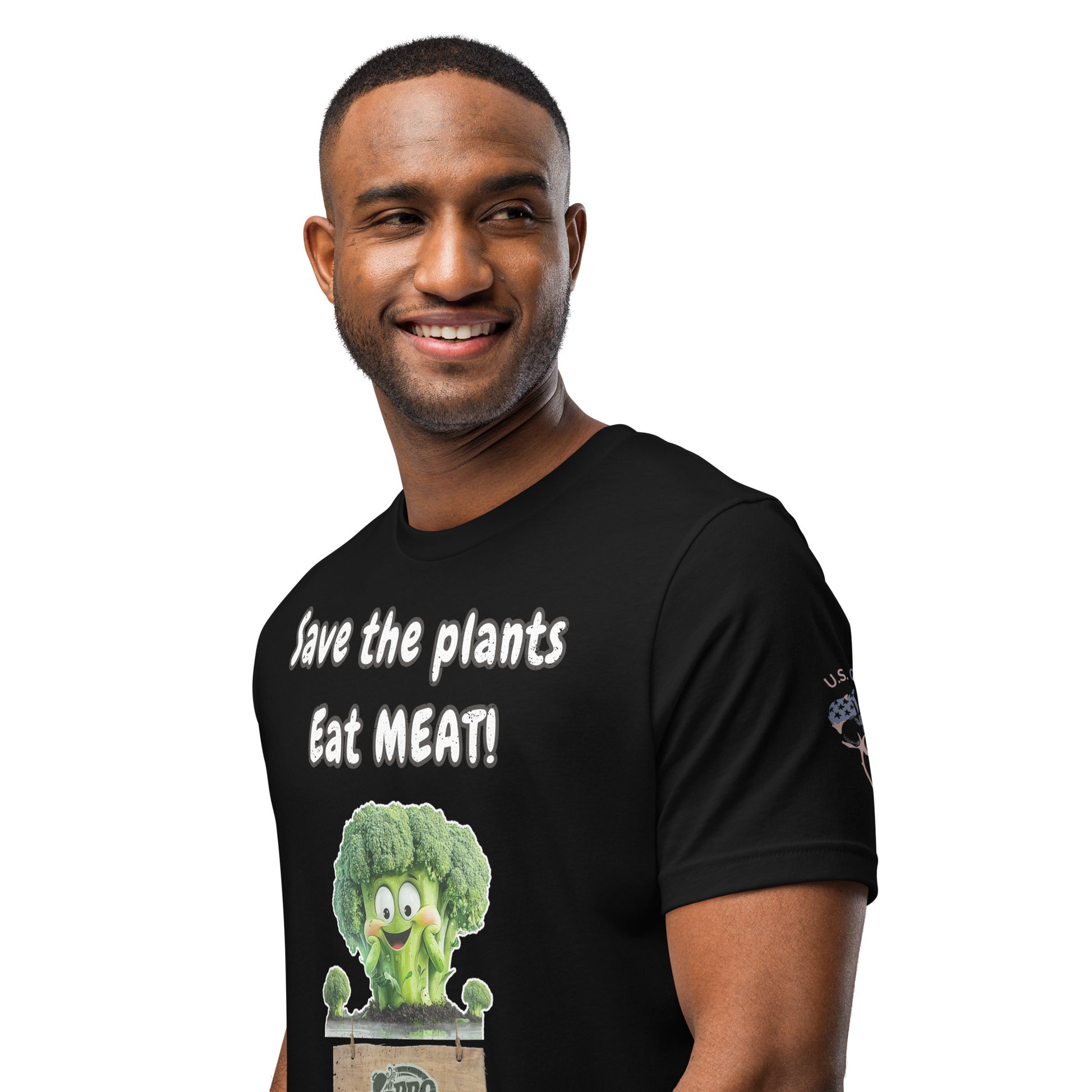 Product mockup. A close-up of a black t-shirt showing a smiling cartoon broccoli in a crate, the phrase "Save the plants Eat MEAT!", and a "U.S. Cotton" badge on the sleeve.