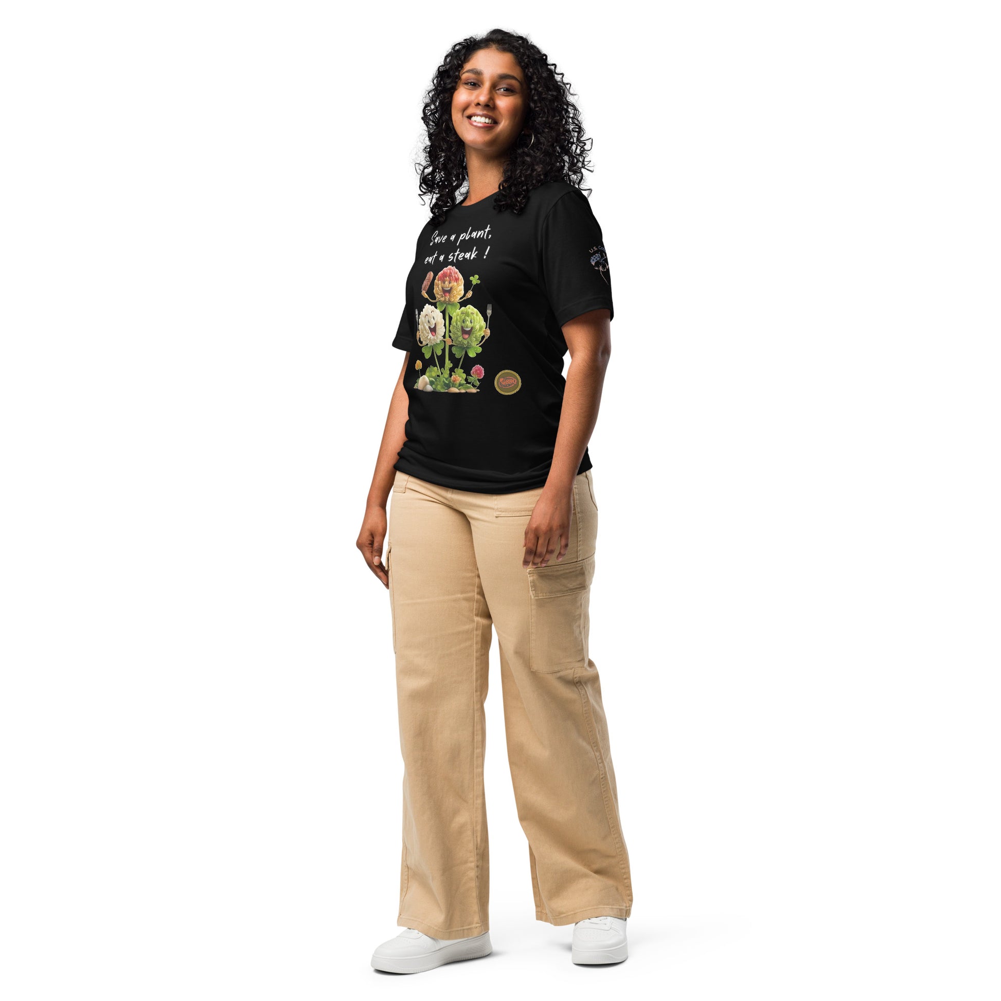 Product mockup. A woman wears a black t-shirt featuring three smiling clover characters, cutlery, and the message "Save a plant, eat a steak!" on the chest, along with a "U.S. Cotton" emblem on the sleeve.