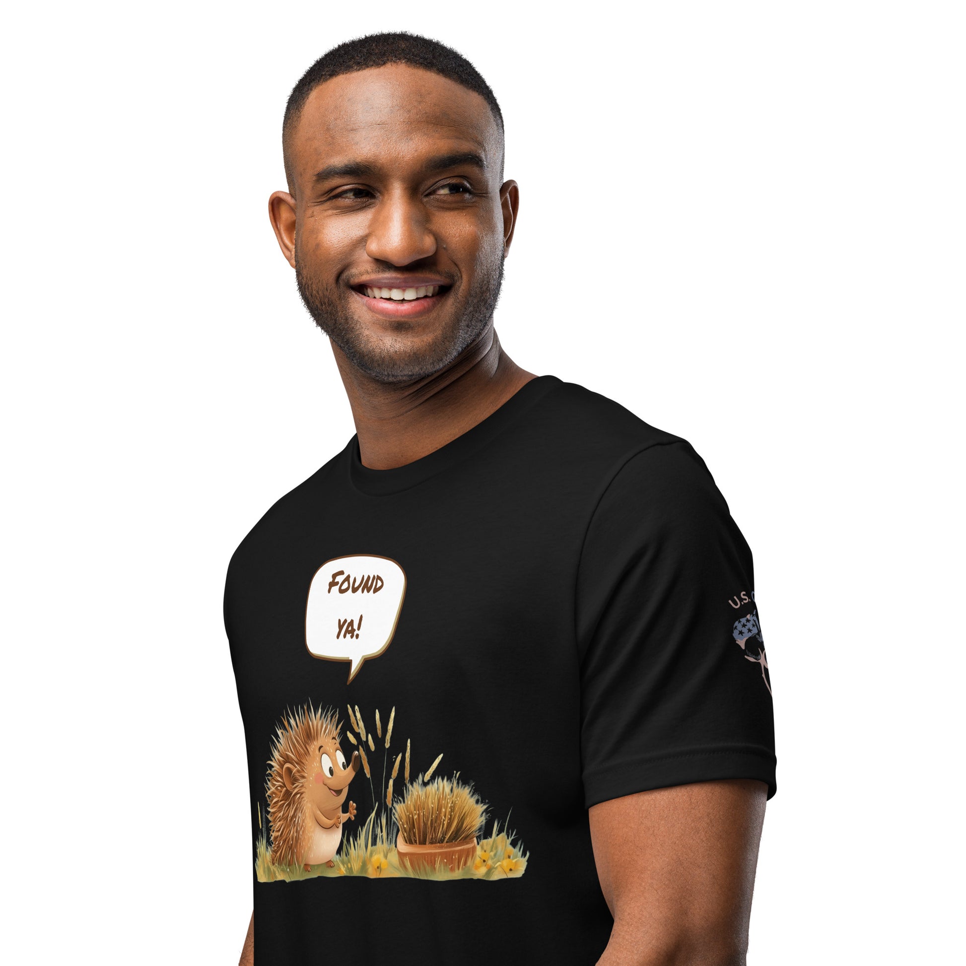 Product mockup. A man wears a black t-shirt illustrated with a hedgehog in grass and the speech bubble text "Found ya!".
