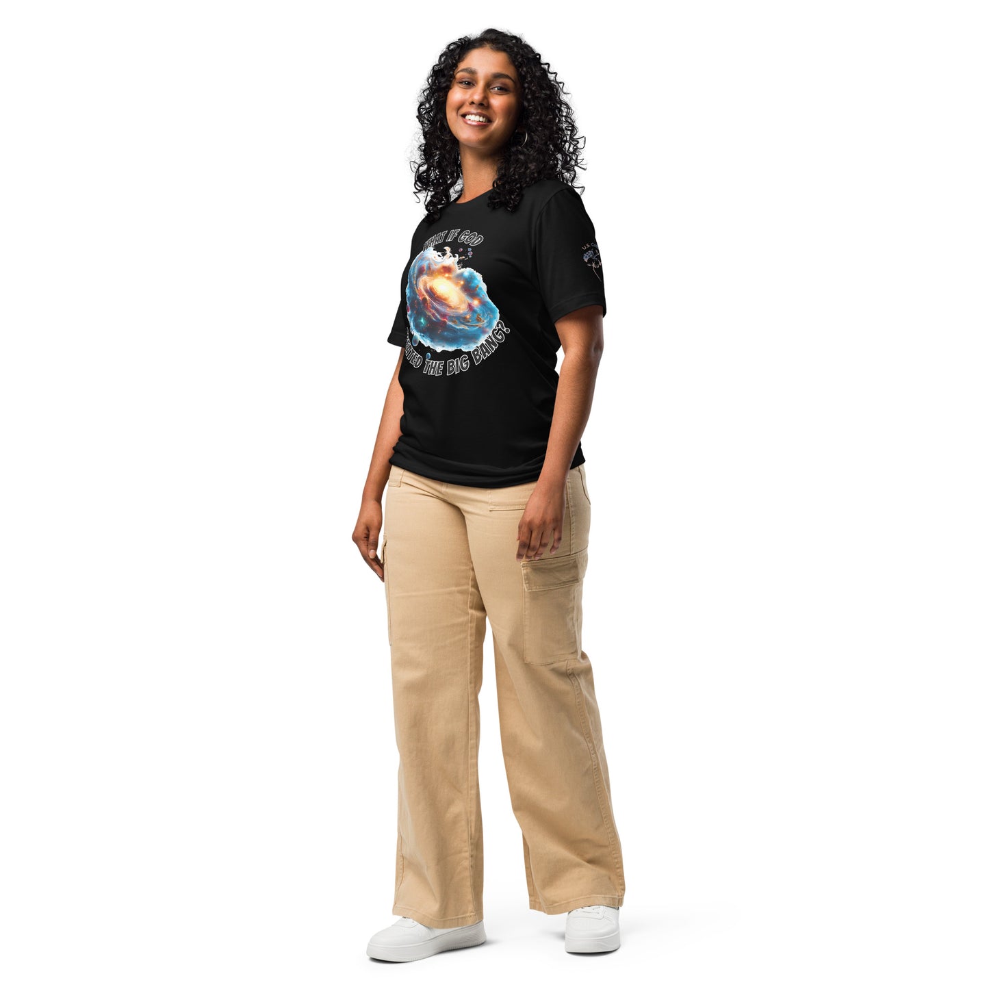Product mockup. A woman dressed in beige pants and a black T-shirt printed with a dramatic cosmic galaxy design and the words “WHAT IF GOD CREATED THE BIG BANG?”, shown in a full-body pose.