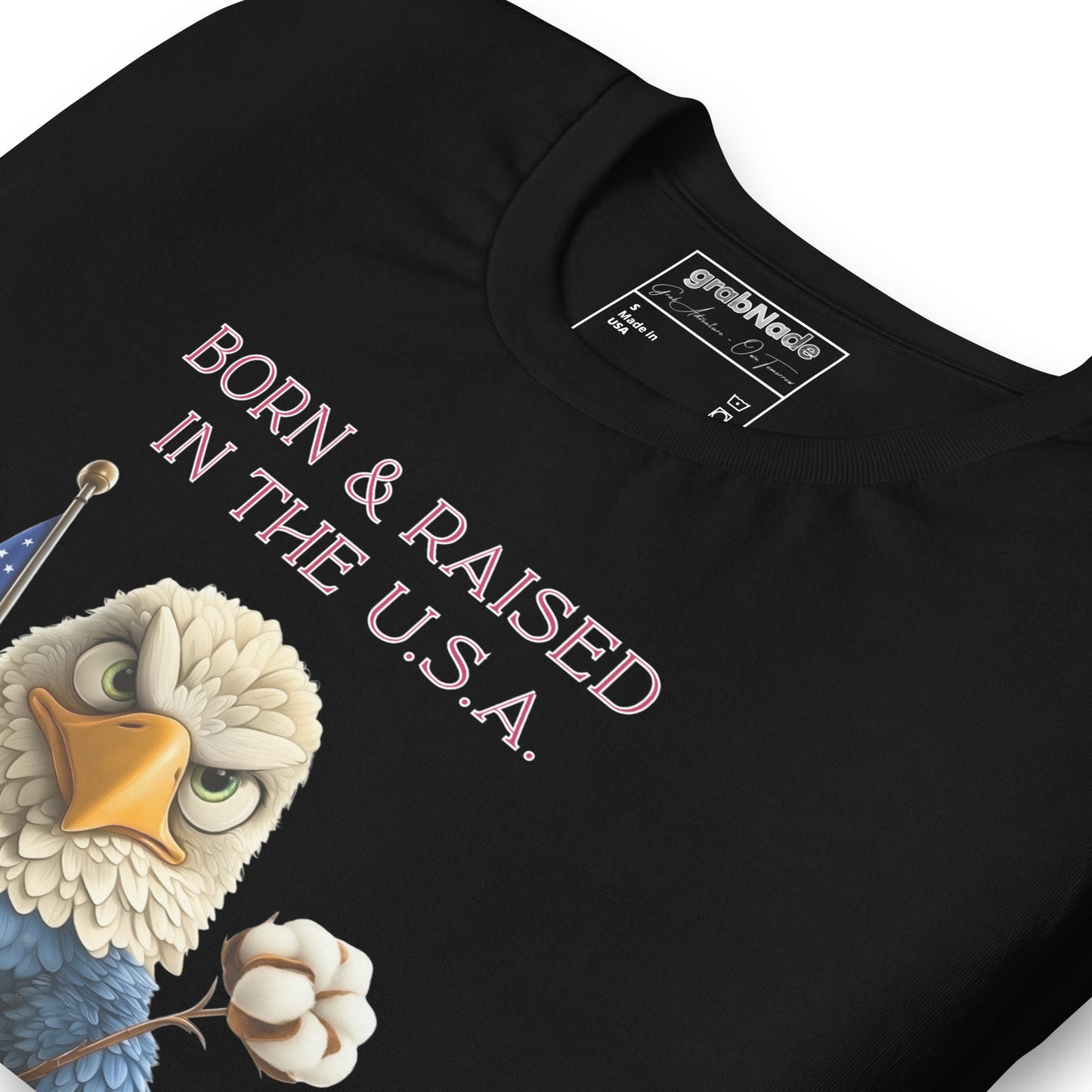 Product mockup. Close-up of a black t-shirt with a cartoon bald eagle holding a cotton boll and the phrase "Born & Raised in the U.S.A."