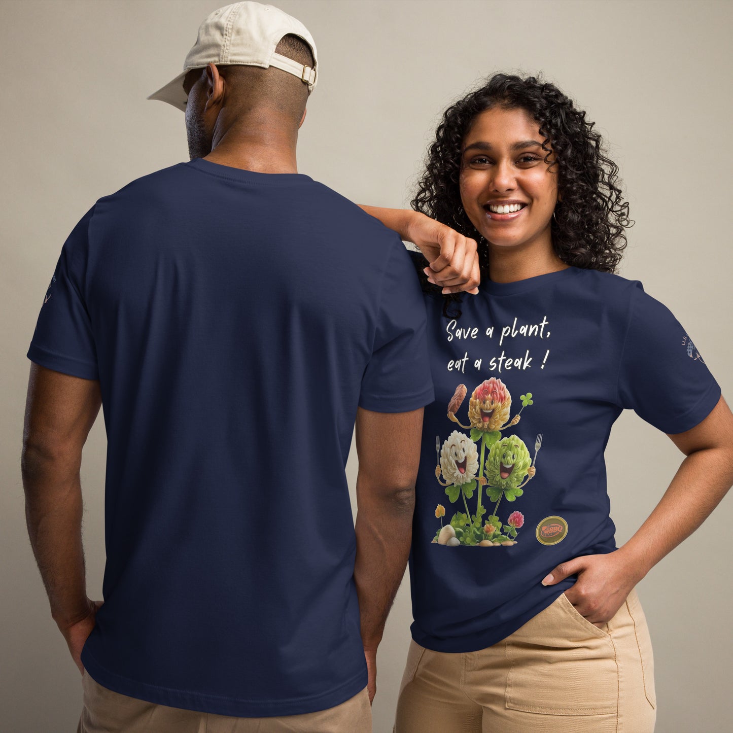 Product mockup. Man and woman in navy t-shirts; man with his back showing, woman smiling in beige pants, displaying a shirt with cartoon flowers and “Save a plant, eat a steak!”.