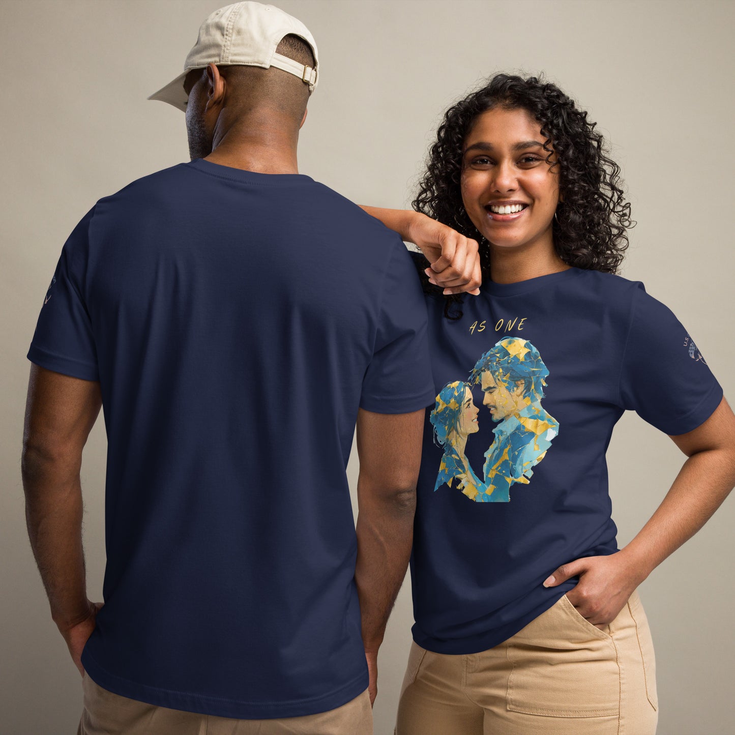 Product mockup. Man and woman; man with back view in navy shirt, woman smiling, both in beige pants. Her shirt shows a blue and gold painted couple with “AS ONE”, man with plain balck view.