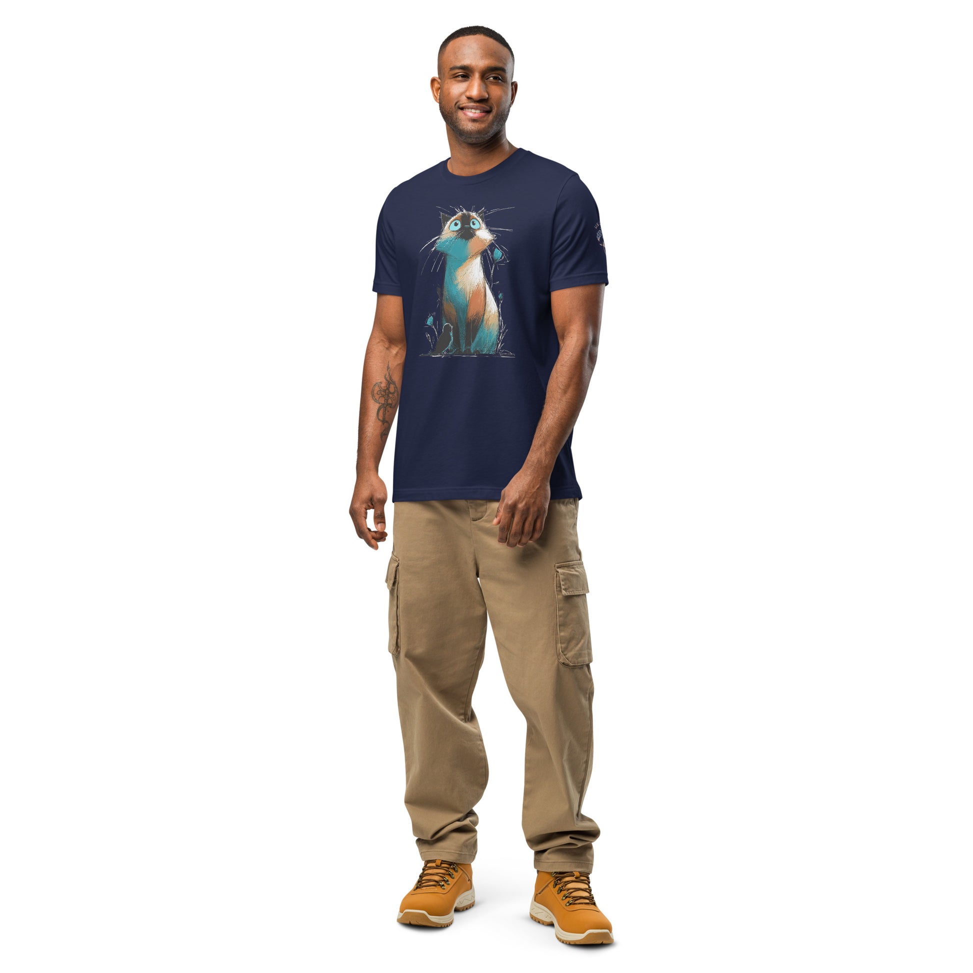 Product mockup. Smiling man in a navy blue t-shirt with a whimsical Siamese cat illustration and blue eyes, surrounded by blue buds, standing in beige cargo pants.