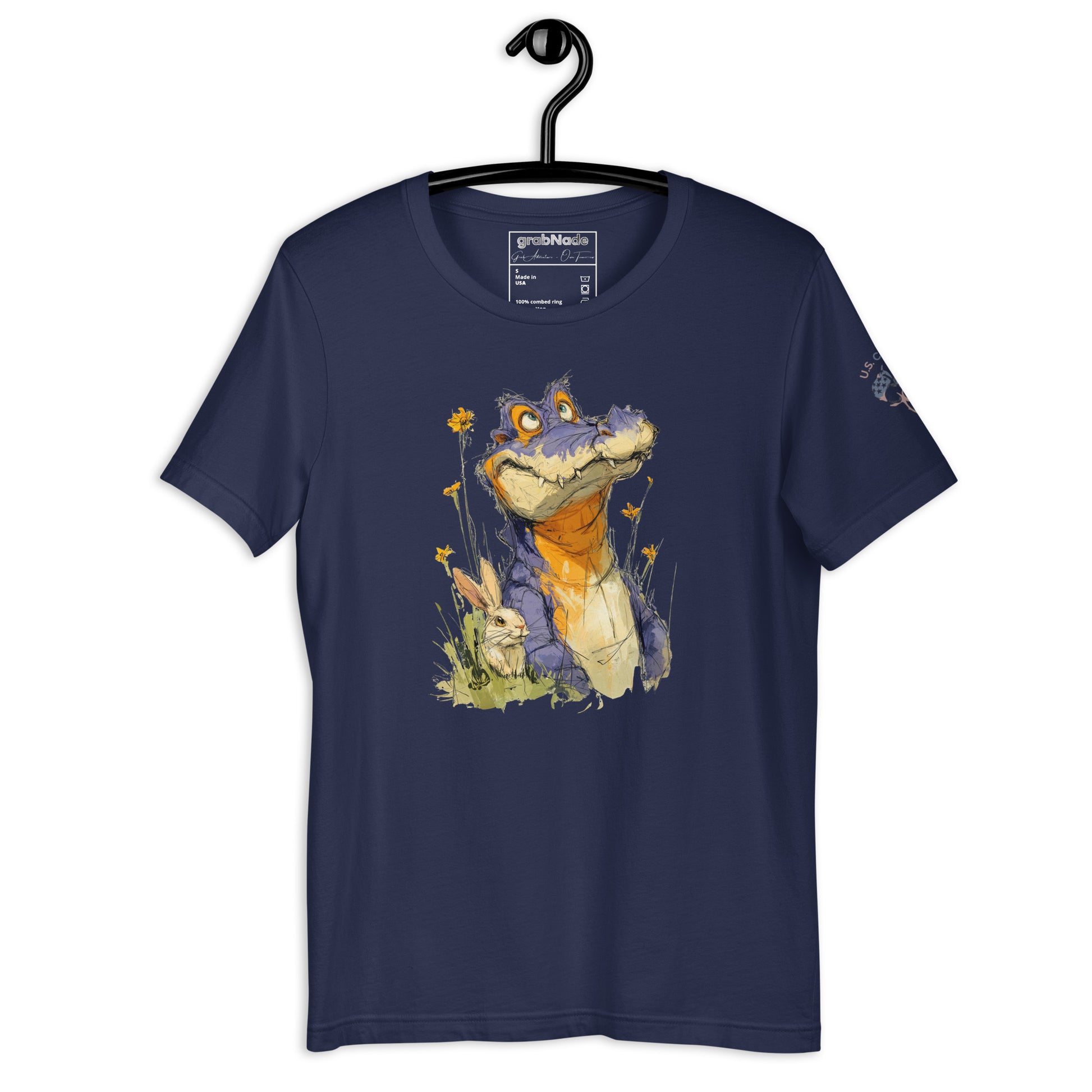 Product mockup. Navy blue t-shirt on a hanger, featuring a whimsical purple cartoon alligator sitting in grass with yellow flowers and a small bunny.