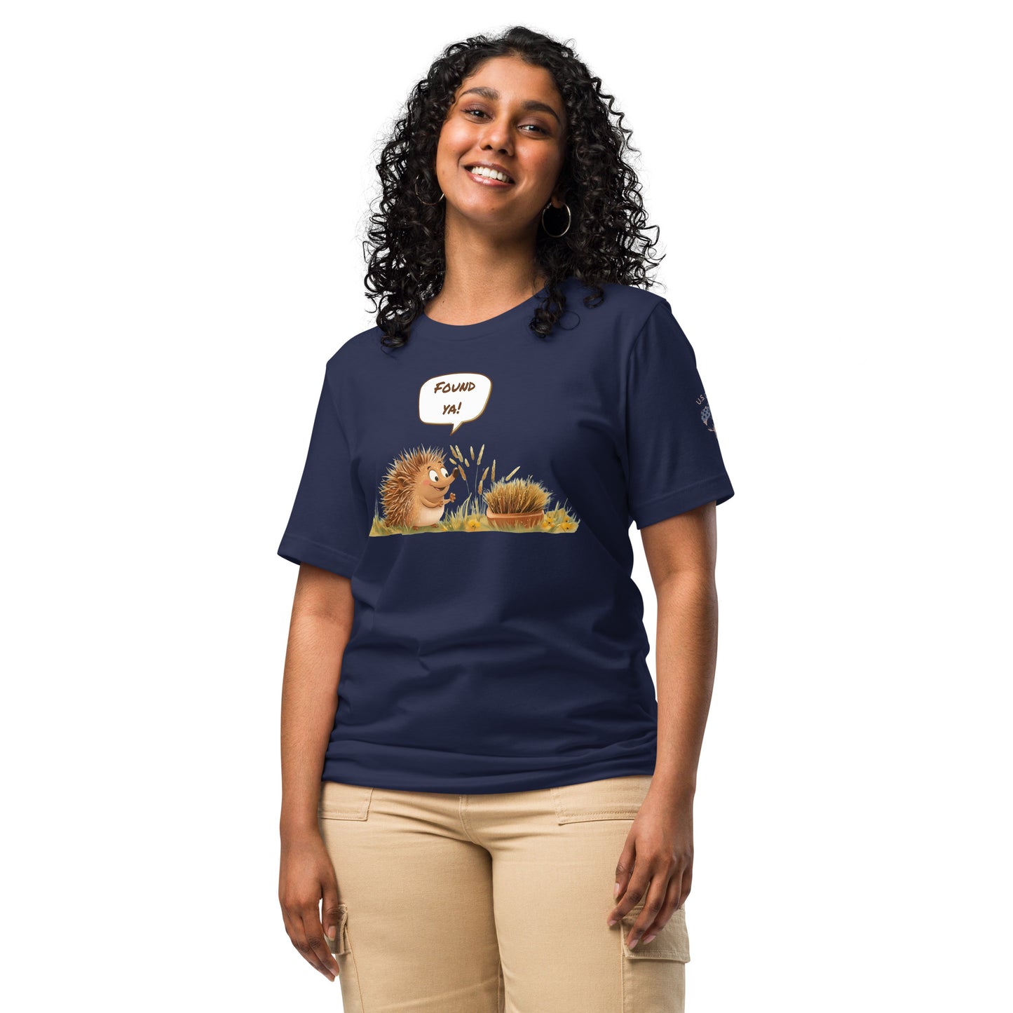 Product mockup. Woman in beige pants wearing a navy blue T-shirt with two illustrated hedgehogs, one exclaiming in a speech bubble “Found ya!”
