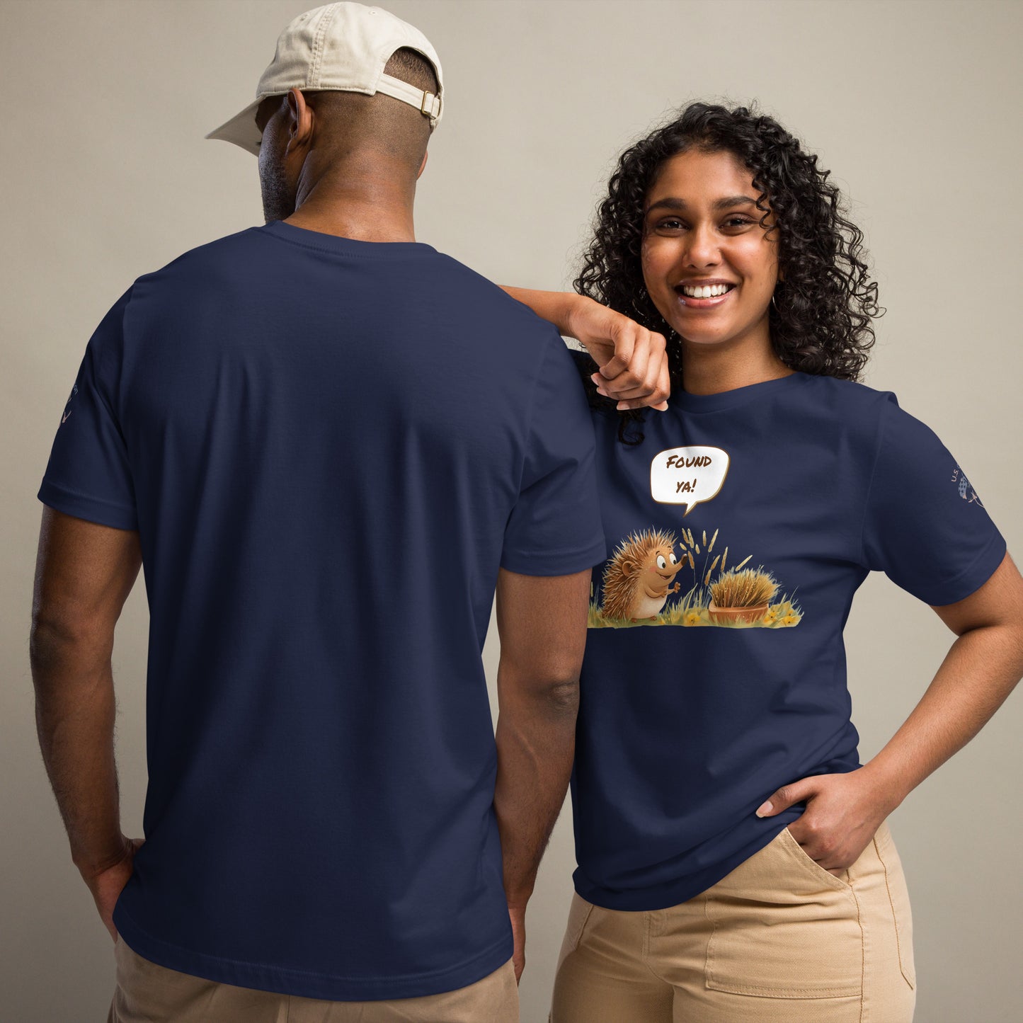 Product mockup. Man and woman in navy blue t-shirts; woman in beige pants, shirt printed with two hedgehogs in a field, one saying “FOUND YA!”, man with back view.