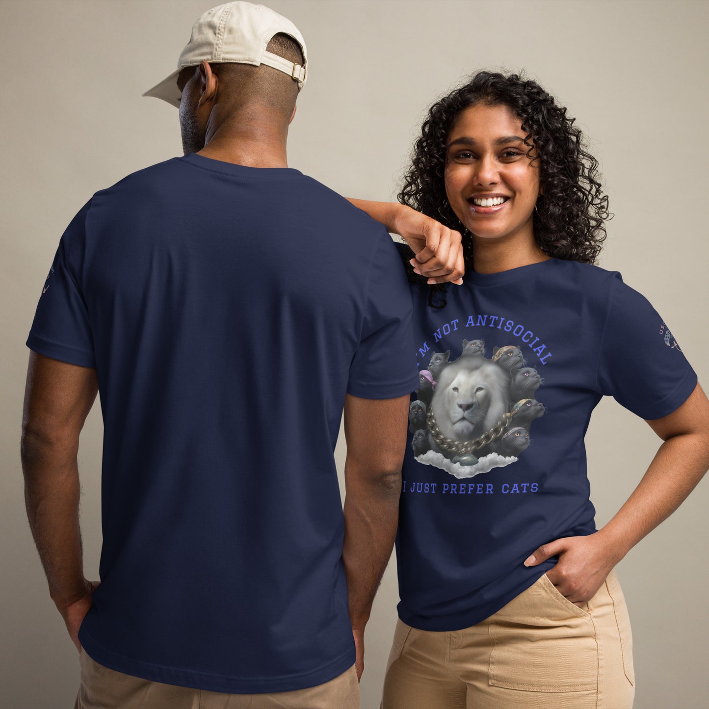 Product mockup. Man and woman in navy t-shirts; man has back view, woman in beige pants. Her shirt shows a white lion surrounded by black cats, with “I’M NOT ANTISOCIAL I JUST PREFER CATS”.