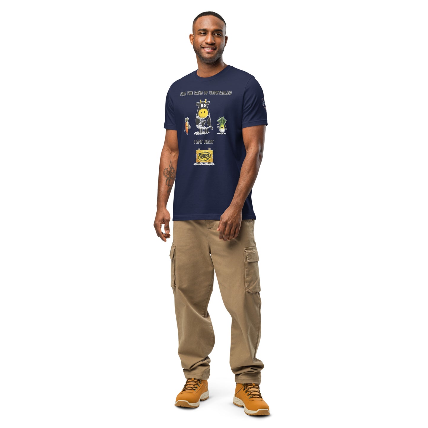Product mockup. Smiling man in beige cargo pants, navy t-shirt with cartoon cow, carrot, lettuce, and BBQ sign, text: “FOR THE SAKE OF VEGETABLES I EAT MEAT”.