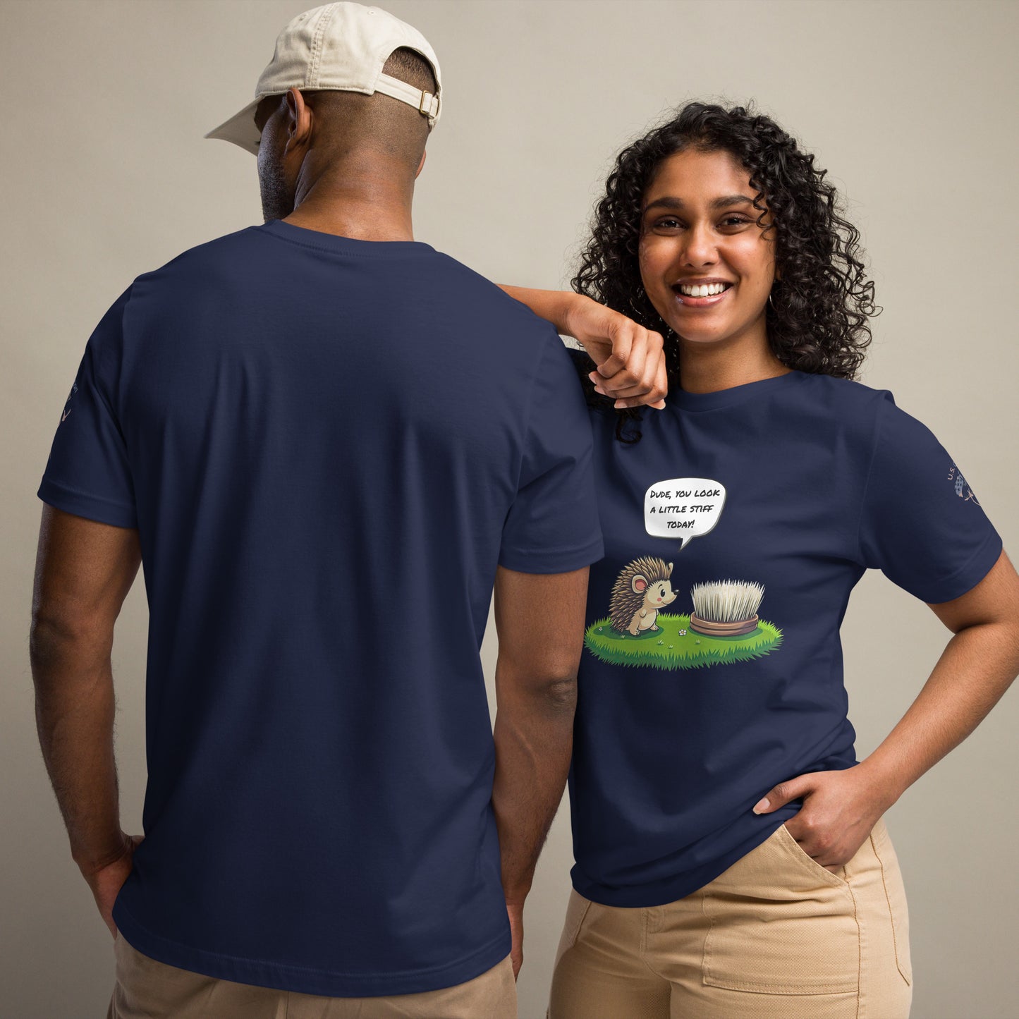 Product mockup. Man and woman in navy blue t-shirts; woman in beige pants, shirt printed with a cute cartoon hedgehog looking at a stiff brush, speech bubble: “DUDE, YOU LOOK A LITTLE STIFF TODAY!” Man’s back view.