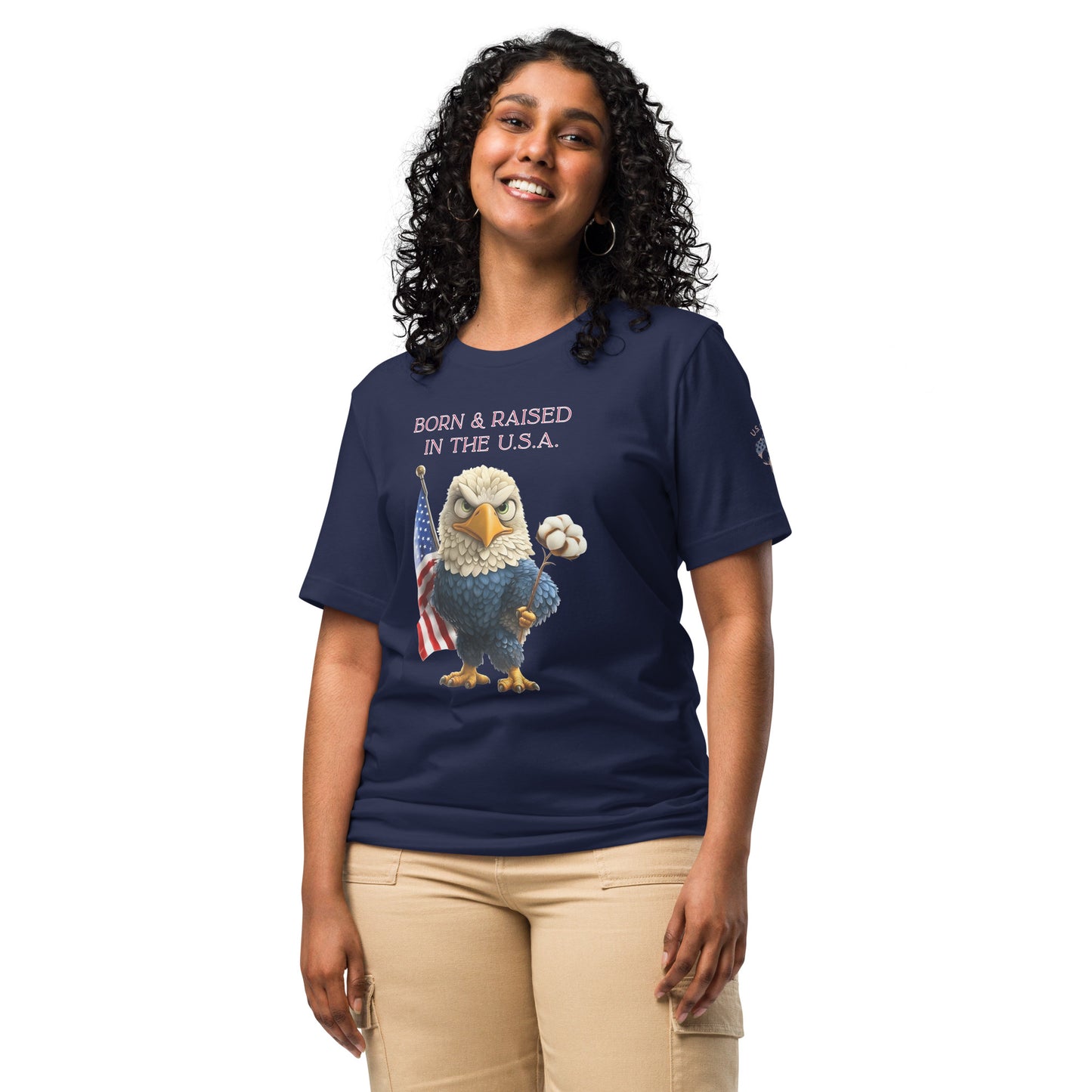 Product mockup. Smiling woman in beige pants and navy blue t-shirt with a cartoon bald eagle holding an American flag and a cotton boll. Text: “BORN & RAISED IN THE U.S.A.”