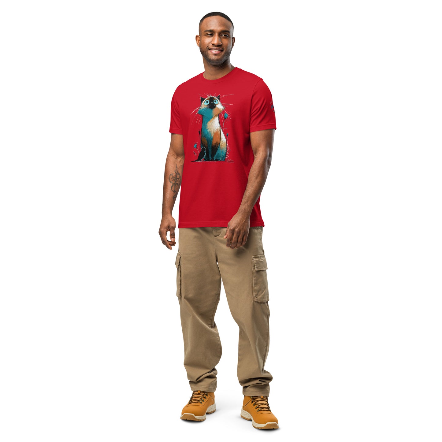 Product mockup. Man in red T-shirt with cartoon-style, wide-eyed cat illustration sitting among abstract grass and flowers.
