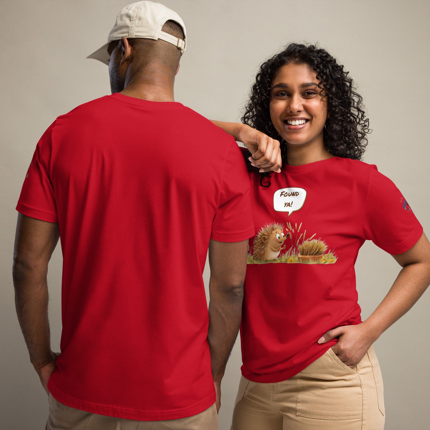 Product mockup. Woman in red T-shirt, cartoon hedgehog pointing at disguised brush, speech bubble: "FOUND YA!"—man has plain back view.