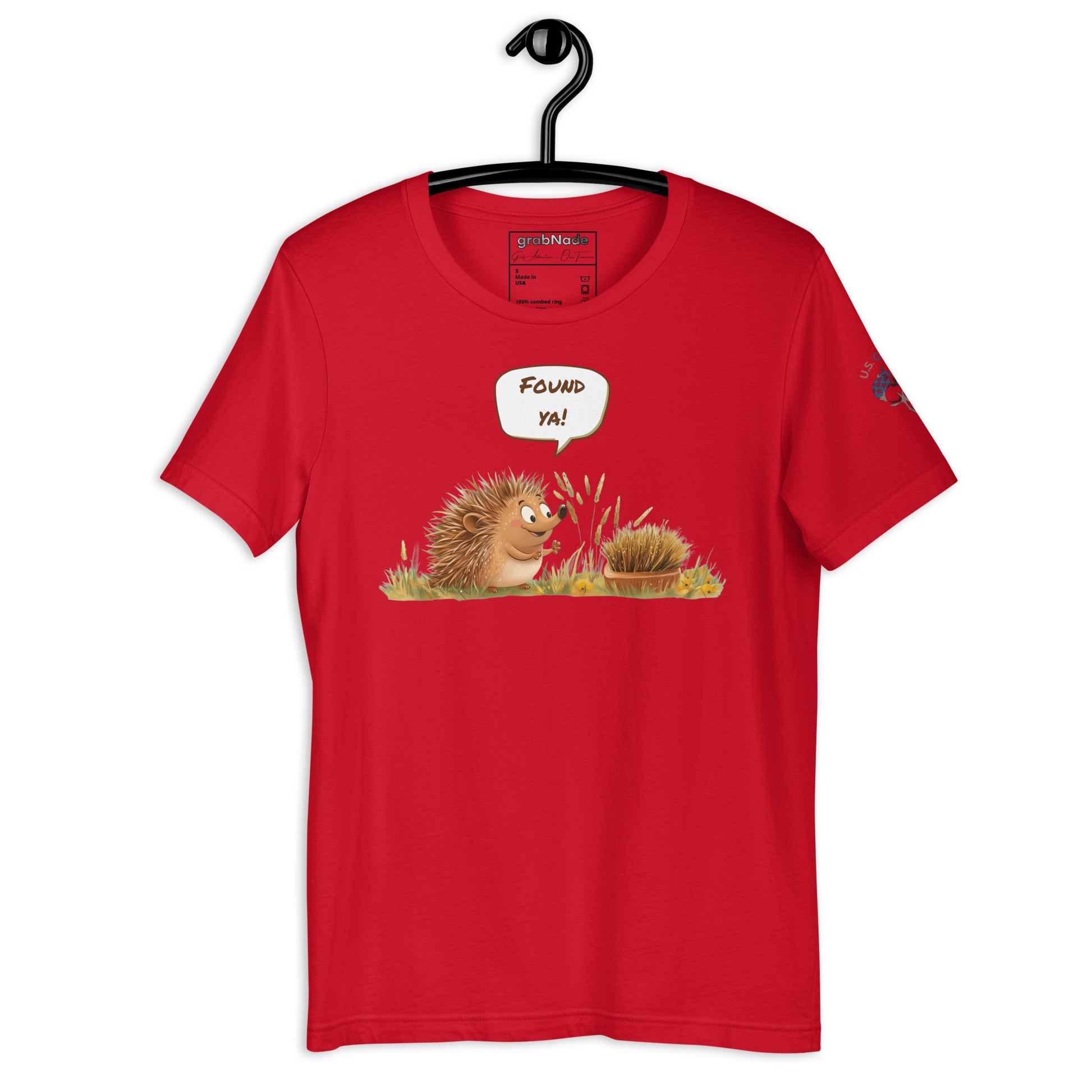 Product mockup. Red T-shirt on hanger, cartoon hedgehog in grass saying "FOUND YA!" to a disguised bundle of bristles.