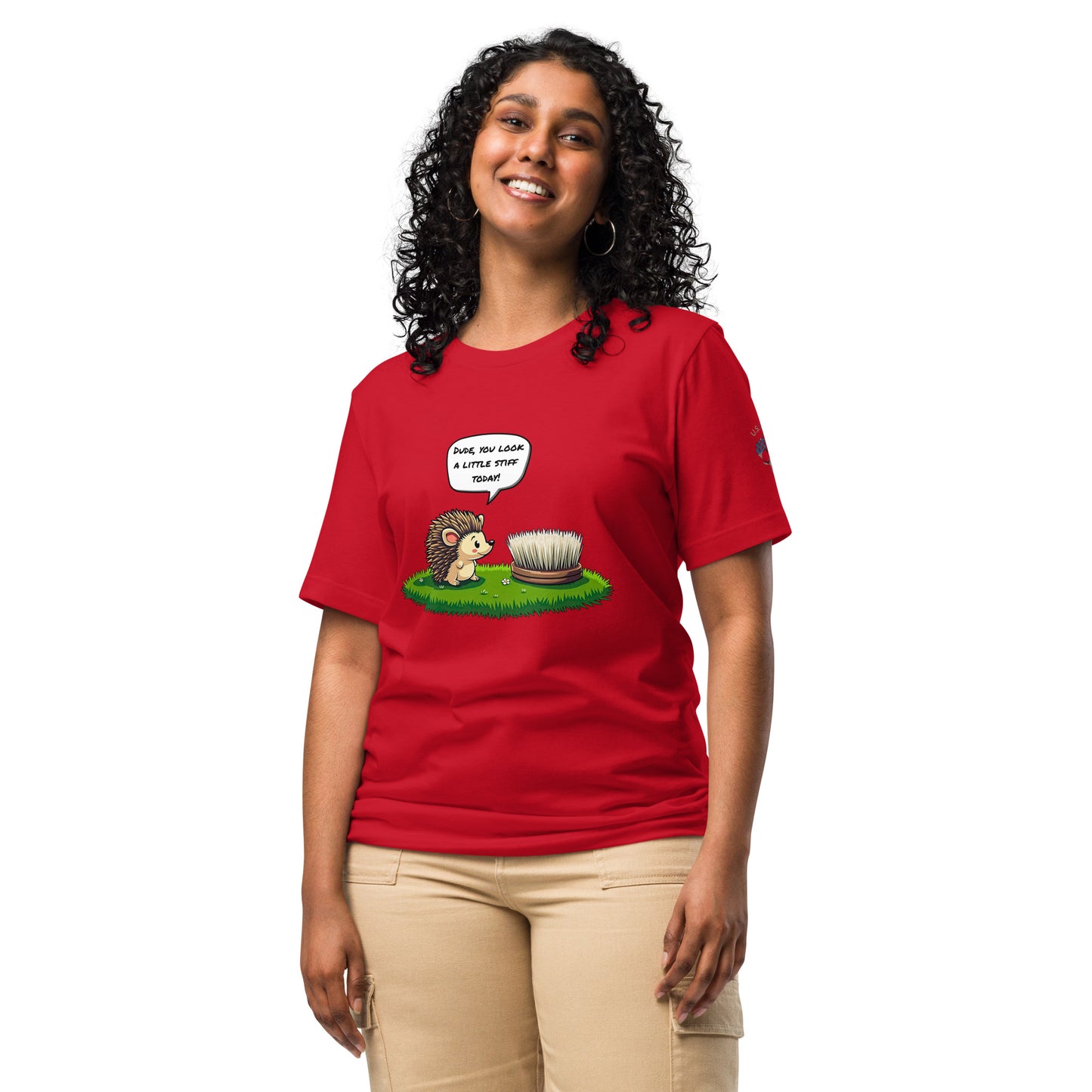 Product mockup. Woman in beige pants wearing a red T-shirt with a hedgehog speaking to a stiff brush in grass, speech bubble says "Dude, you look a little stiff today!"