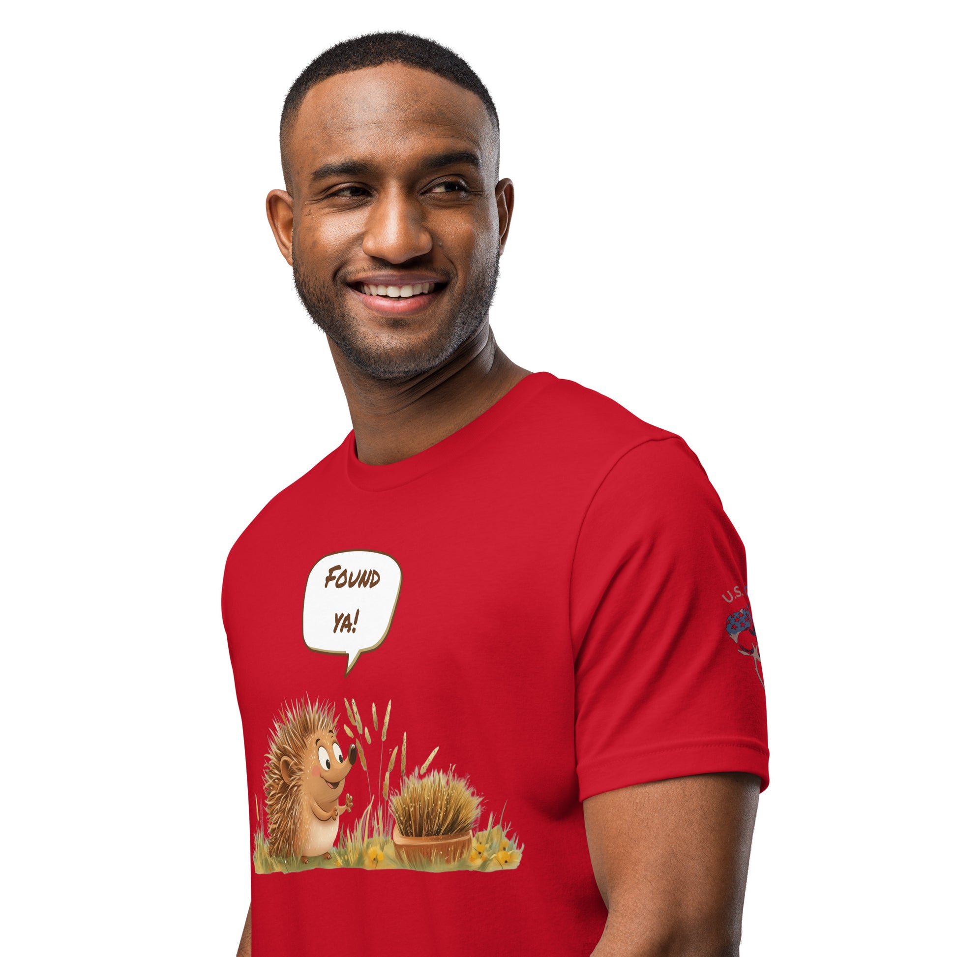 Product mockup. A man in a red T-shirt featuring a cartoon hedgehog saying "Found ya!" to another hedgehog camouflaged as a pile of grass, shown from the waist up.
