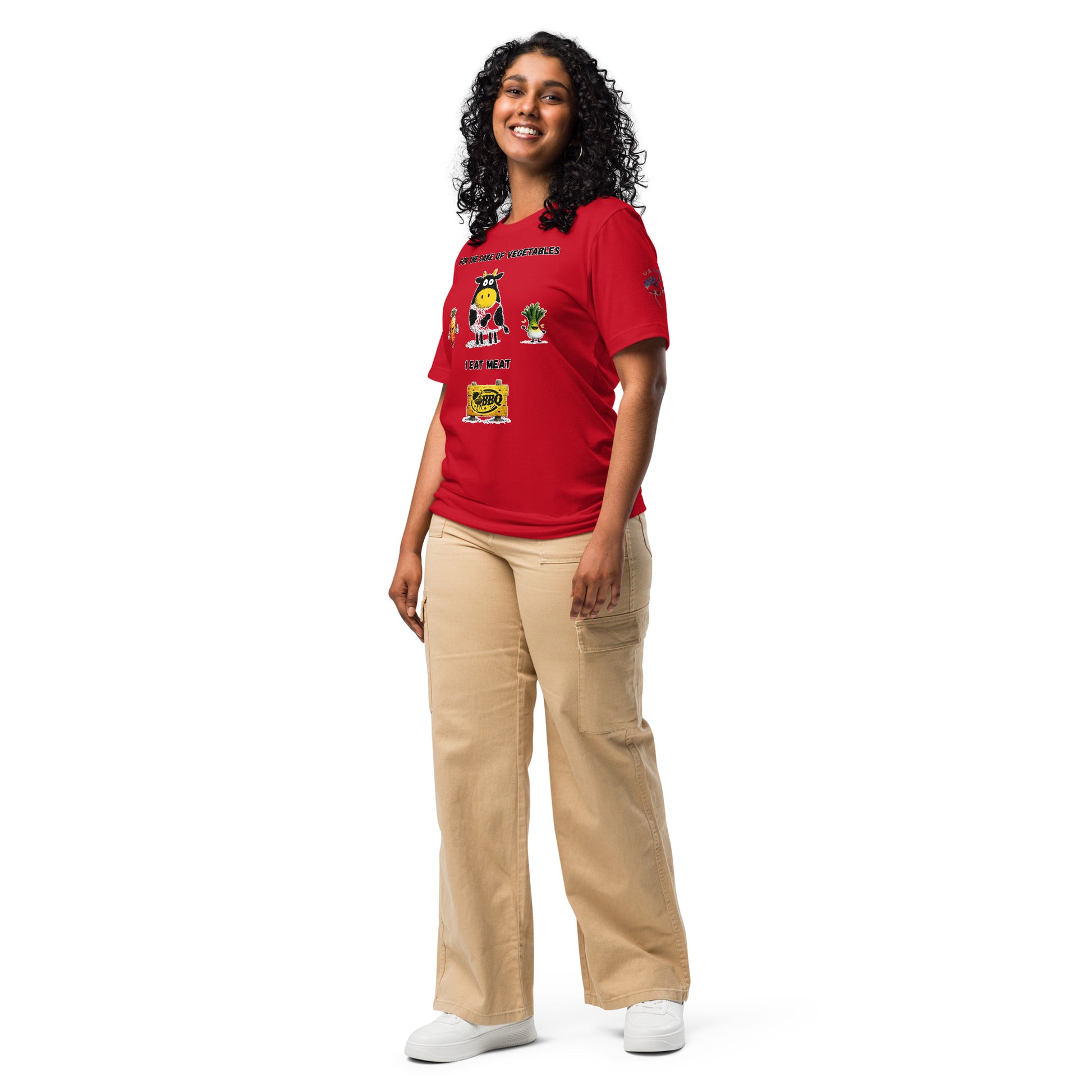 Product mockup. A woman in beige cargo pants and a red T-shirt with playful cartoon characters, including a cow, carrot, and bok choy, and the words “For the sake of vegetables I eat meat,” full-body pose.